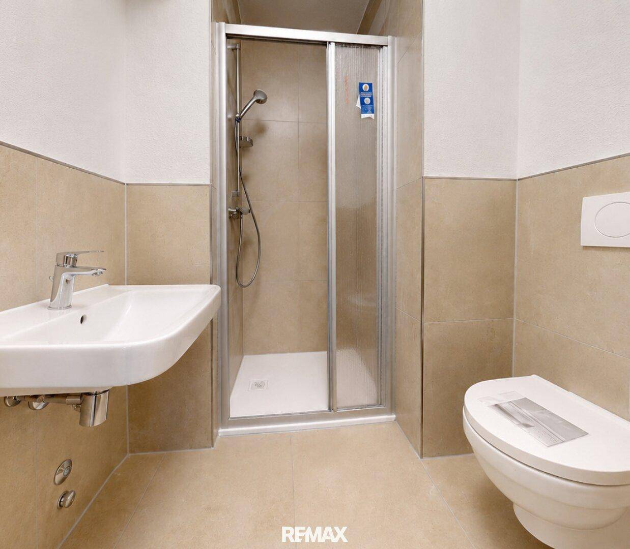 Modernes Badezimmer mit Duschkabine, WC und Waschbecken in neutralen Beigetönen.