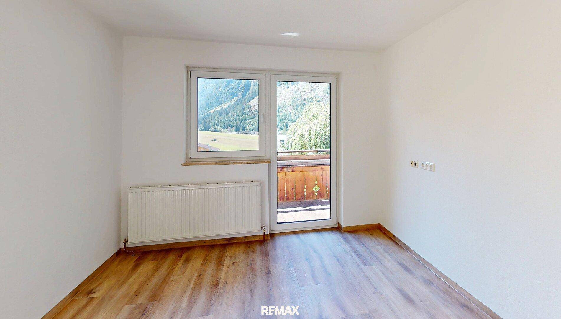 Leerer Raum mit Laminatboden und Balkonzugang, der einen weiten Blick auf die Berge ermöglicht.