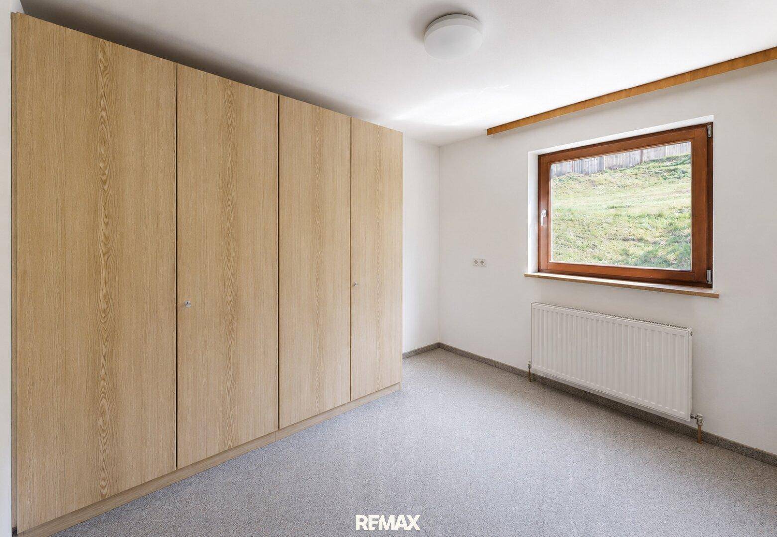 Schlafzimmer mit integrierten Holzschränken, Teppichboden und Fenster mit Blick ins Grüne.
