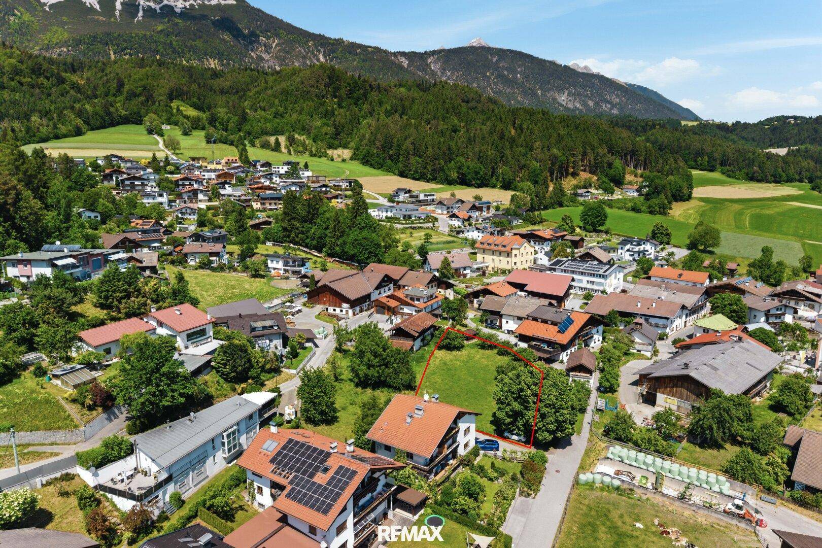 Luftaufnahme eines malerischen Dorfes in den Bergen mit grünen Wiesen und Wäldern, umgeben von einer idyllischen Landschaft.
