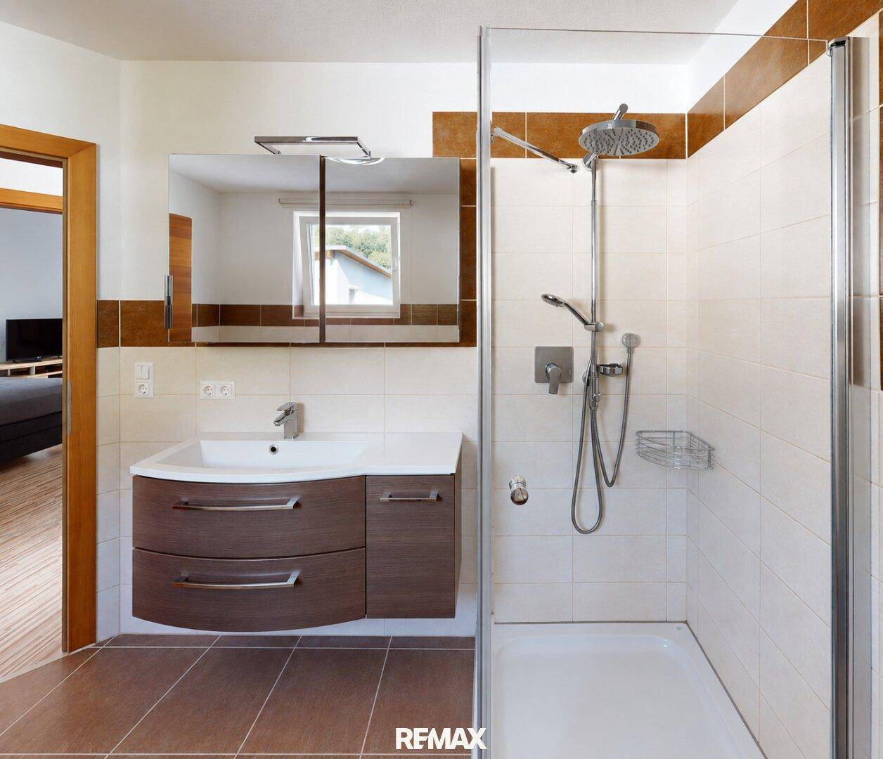 Badezimmer mit moderner Duschkabine, Waschbeckenunterschrank und Spiegelschrank.