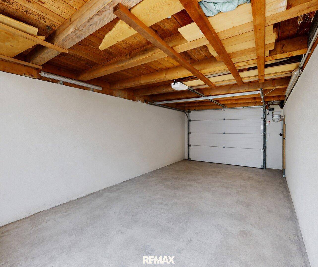 Geräumige Garage mit Betonboden und Holzbalkendecke, bereit zur Nutzung.