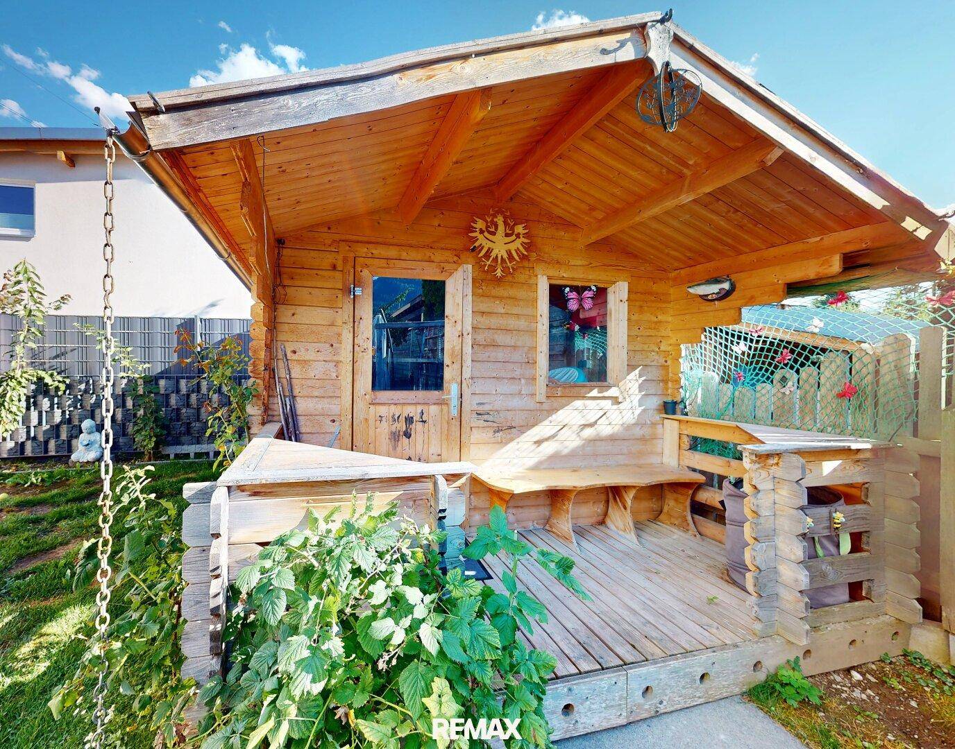 Rustikales Gartenhaus aus Holz mit kleiner Veranda und Sitzgelegenheit im Grünen.