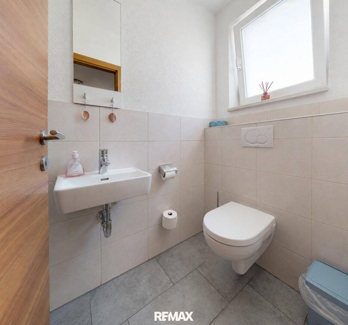 Helles Gäste-WC mit kleinem Waschbecken, wandhängendem WC und Fenster.