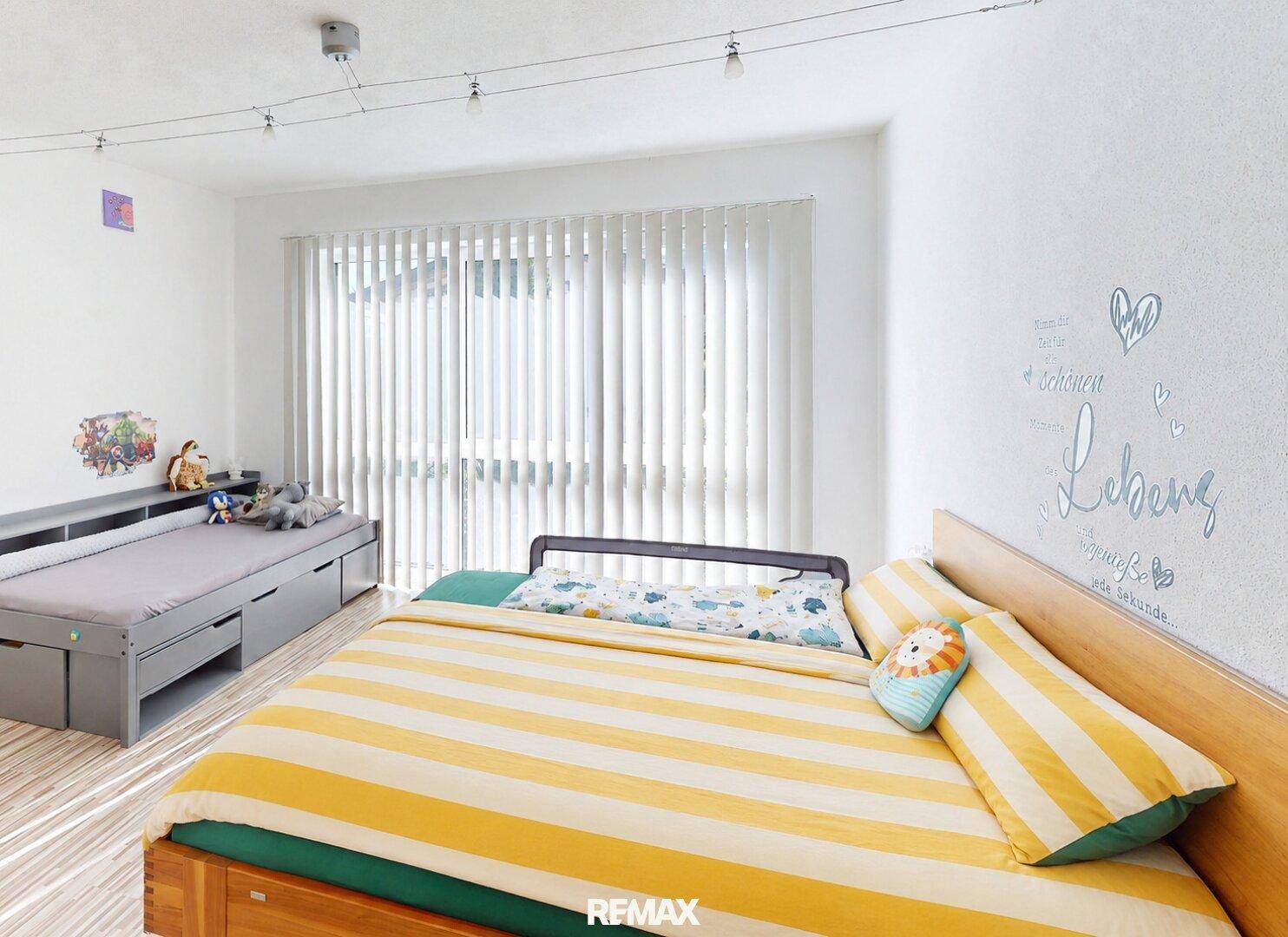 Kinderzimmer mit zwei Betten, Holzboden und hellen Fenstern mit Jalousien.