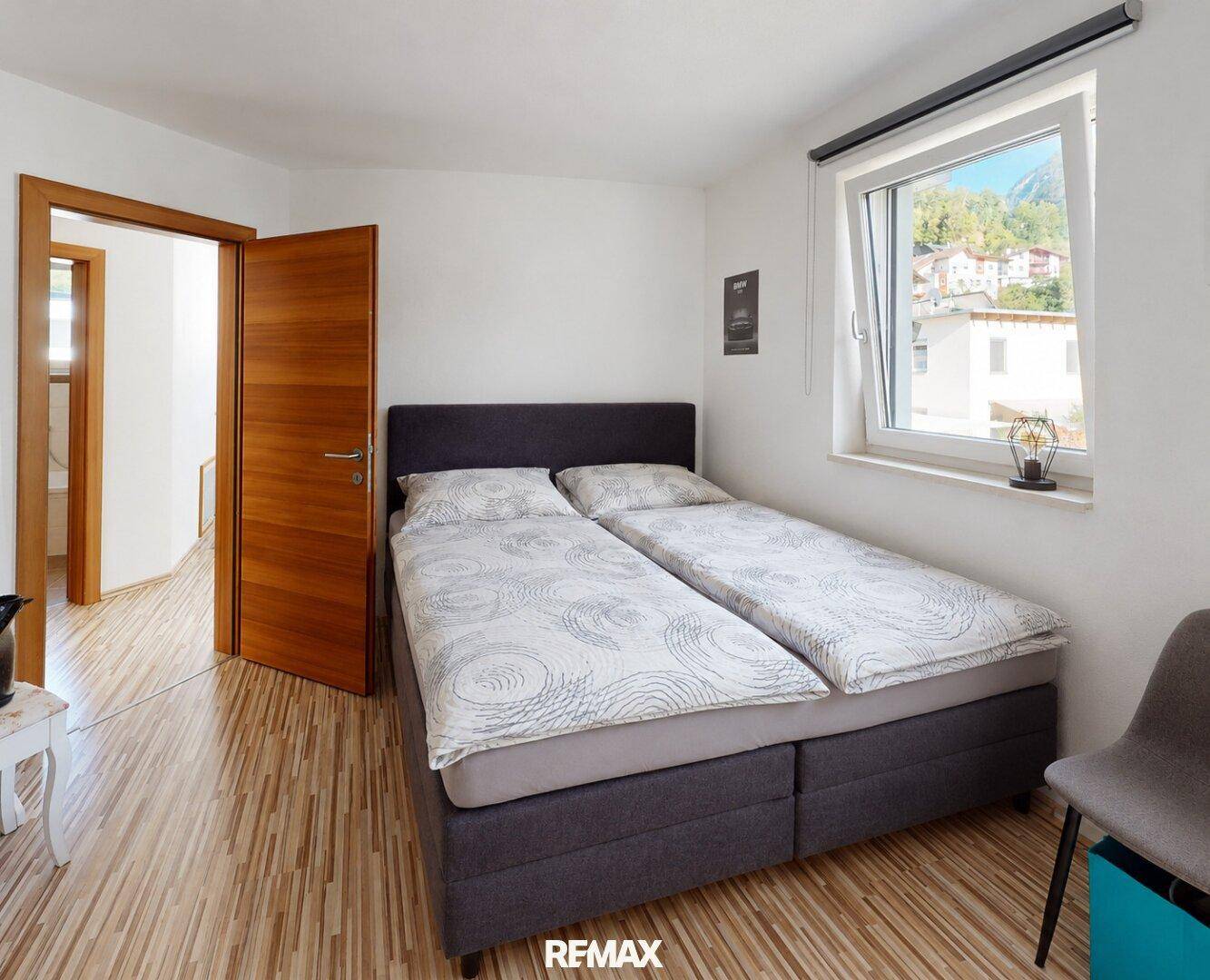 Gemütliches Schlafzimmer mit Doppelbett, Holzboden und Fenster mit Bergblick.