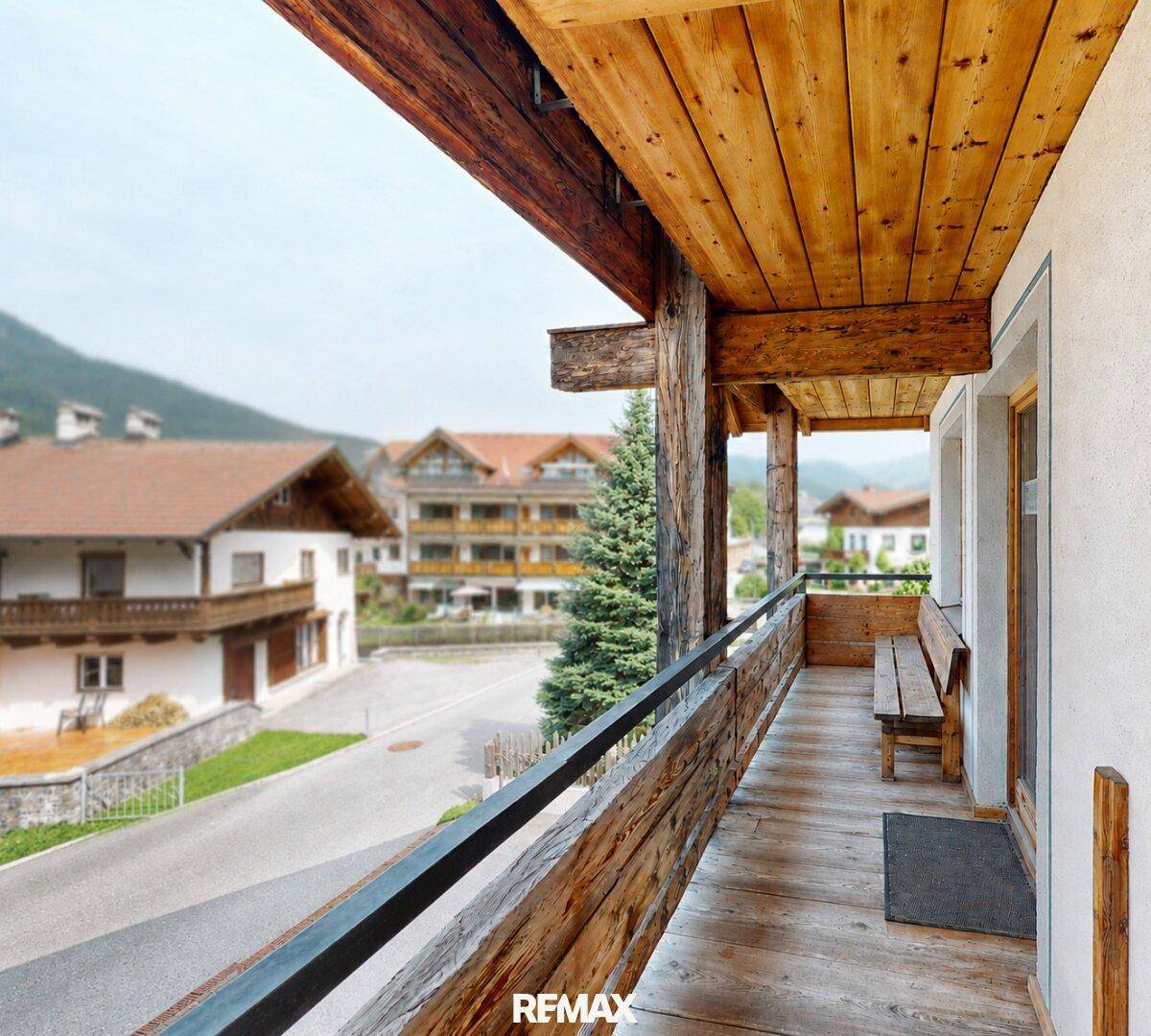 Langer Holzbalkon mit Sitzbank und Blick auf die umliegende Bebauung.