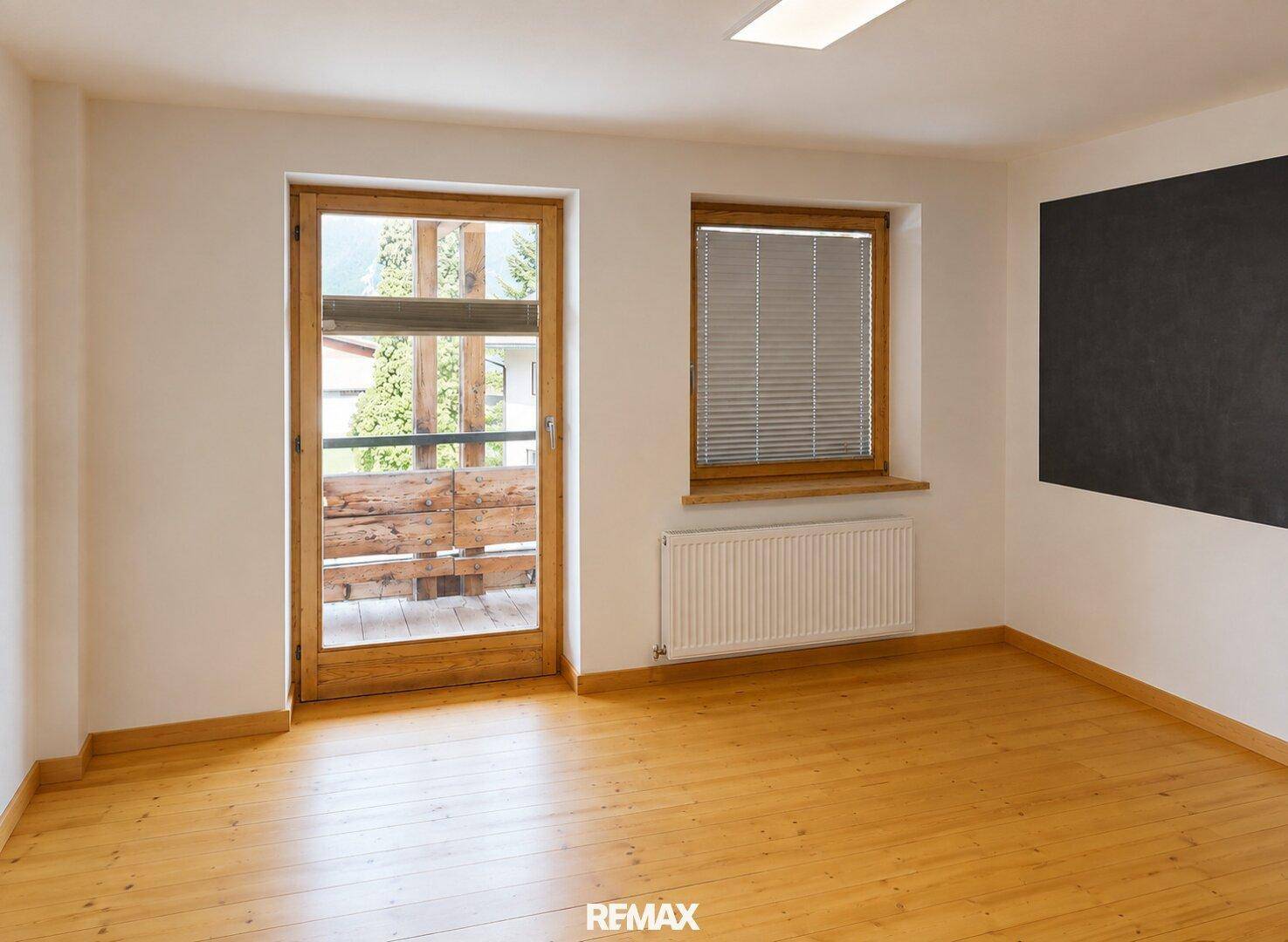 Leerer Raum mit Holzboden, Fenster und Zugang zu einem Balkon.