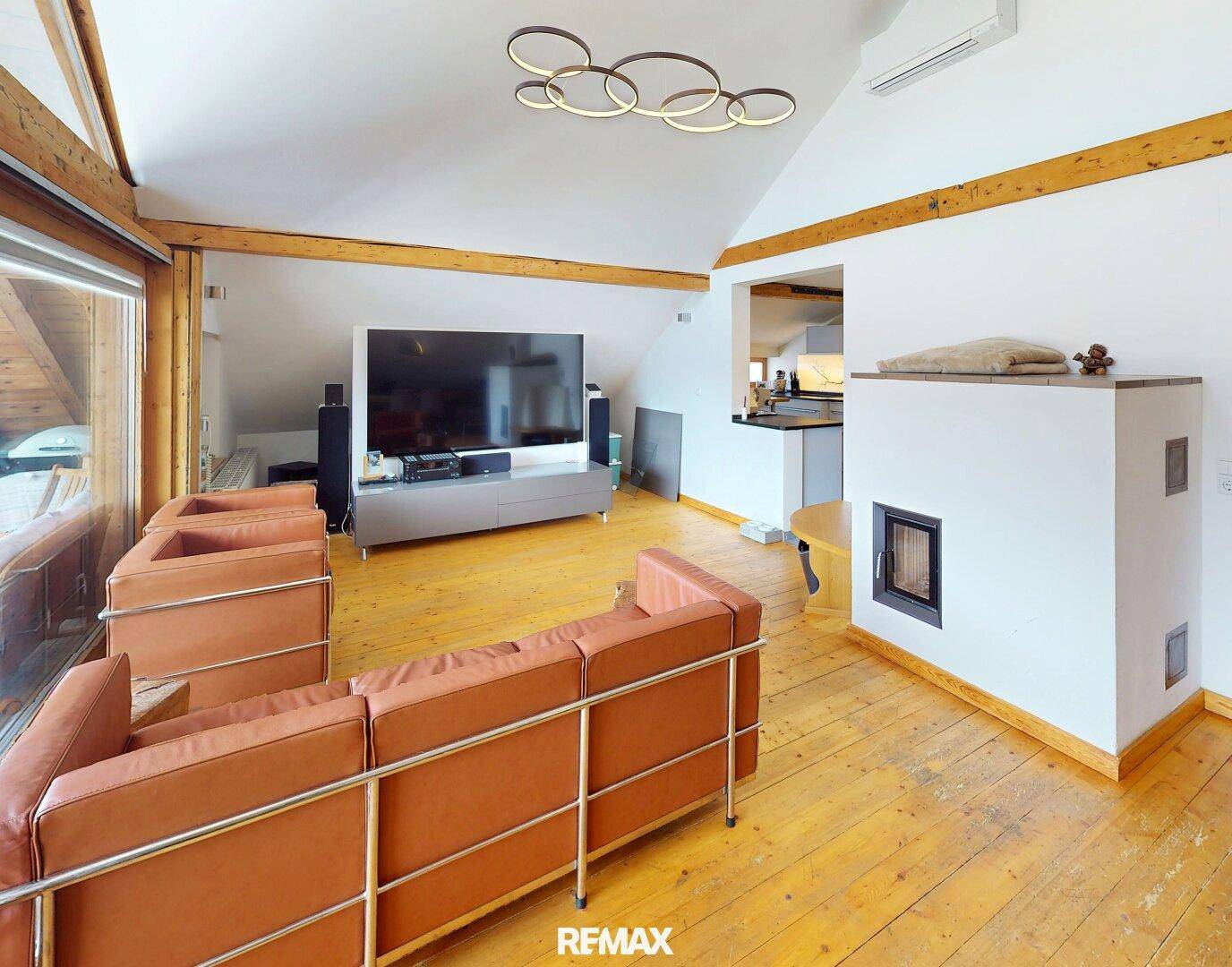 Helles Wohnzimmer mit Kachelofen, Holzbalken und großem Fernseher.