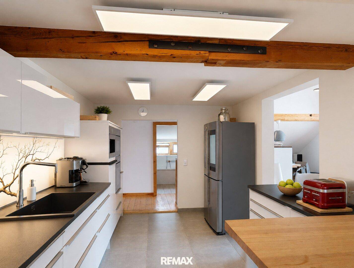 Helle, moderne Küche mit integrierten Geräten, freiliegenden Holzbalken und Fliesenboden.