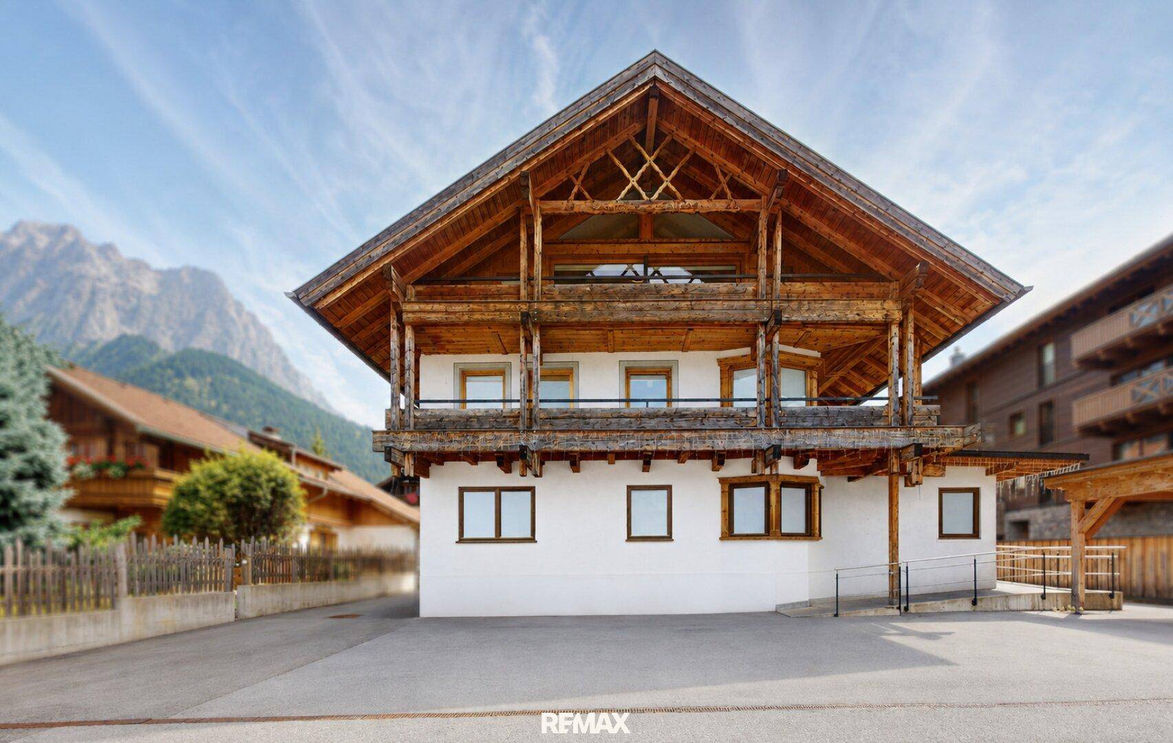 Traditionelles Holzhaus mit weißer Fassade und Bergblick in alpiner Umgebung.