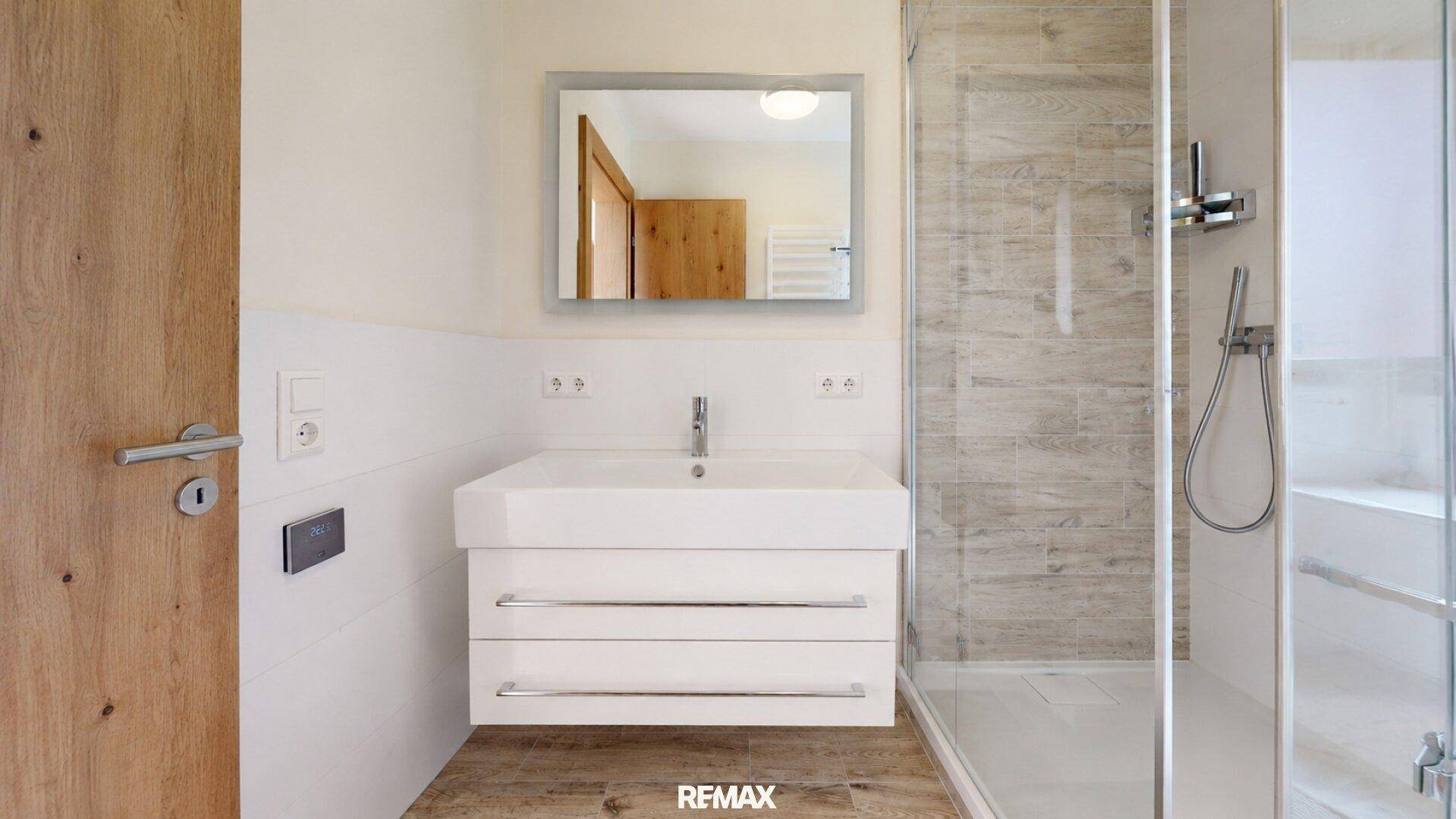 Helles Badezimmer mit modernem Waschbecken, Spiegel und Duschbereich.
