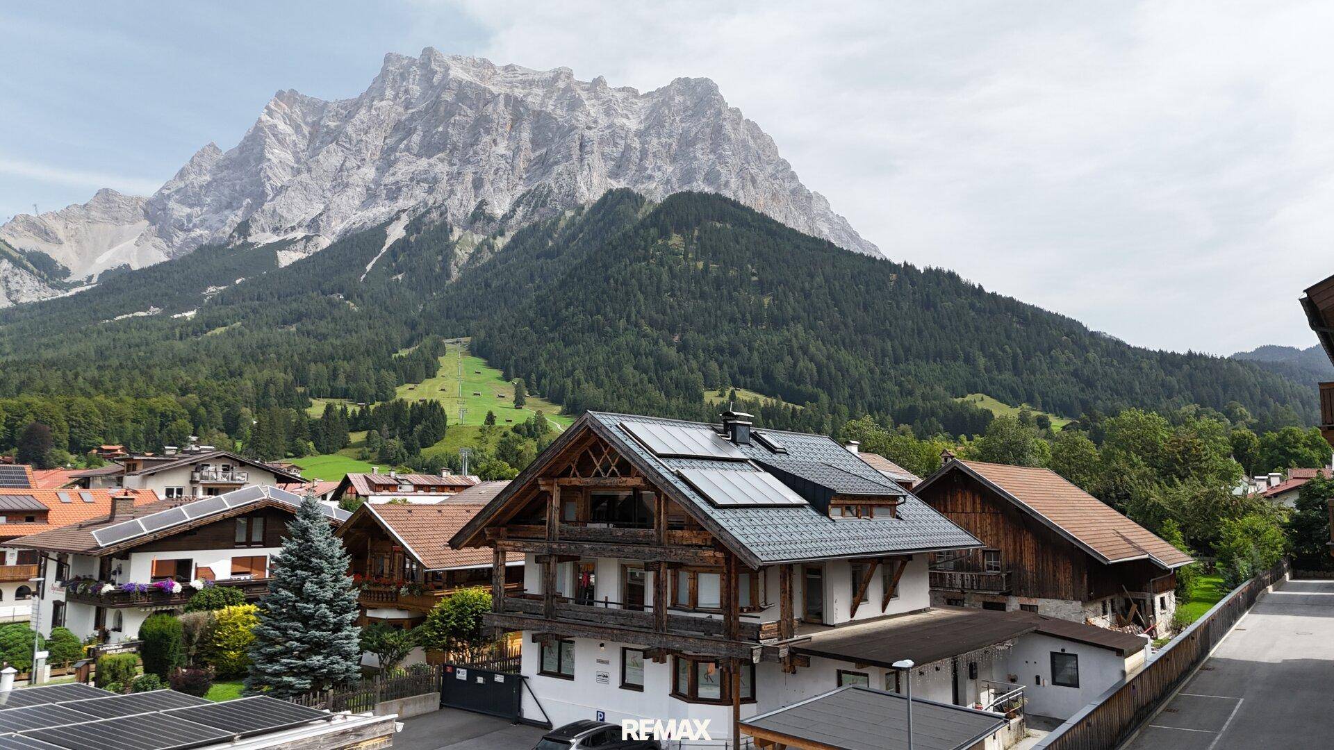 Gebäude im alpinen Stil mit Photovoltaikanlage auf dem Dach und Bergblick.