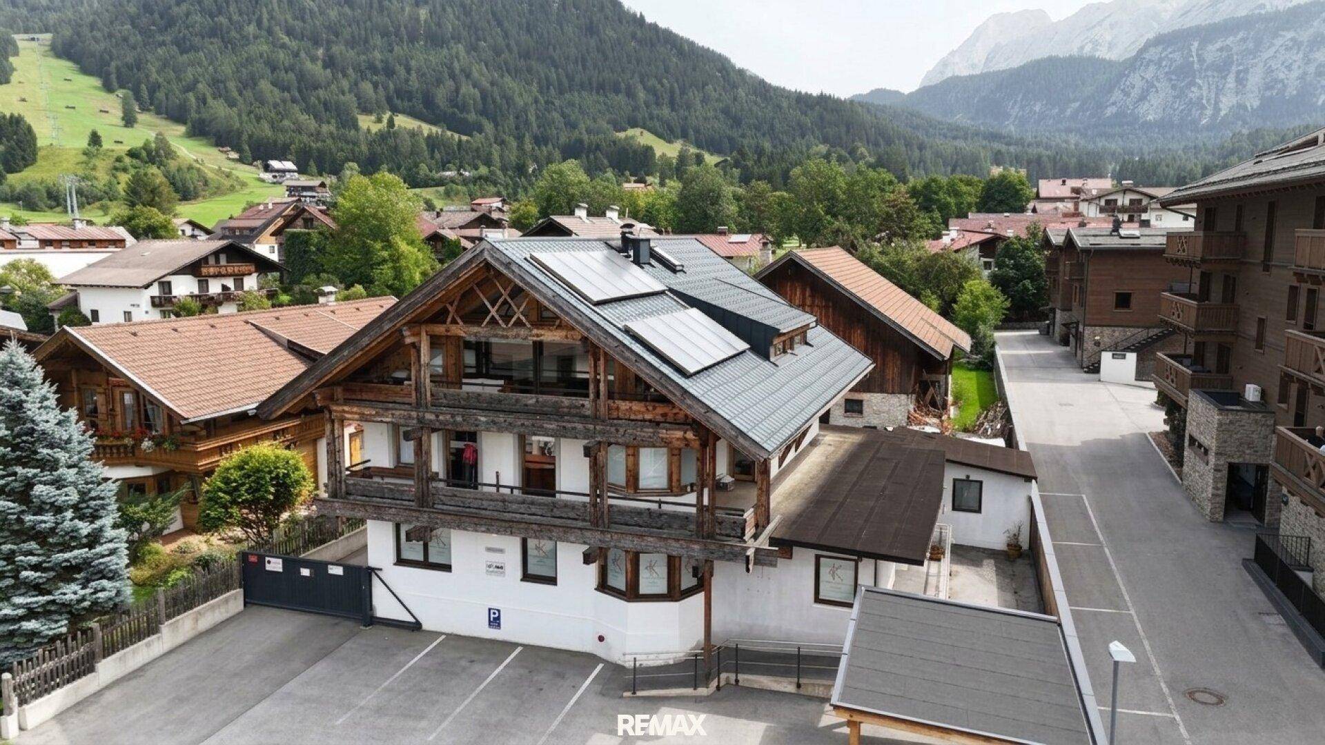 Gebäude im alpinen Stil mit Photovoltaikanlage, Parkplätzen und Bergblick.