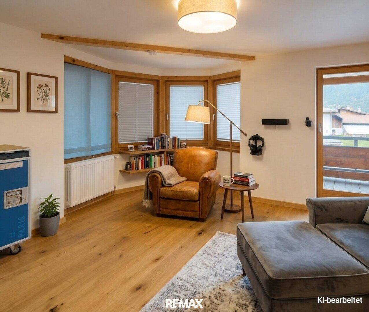 Gemütliches Wohnzimmer mit Ledersessel, Bücherregal und Zugang zum Balkon.