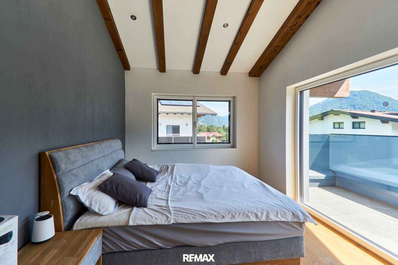 Helles Schlafzimmer mit Holzbalken, Zugang zum Balkon und Bergblick.