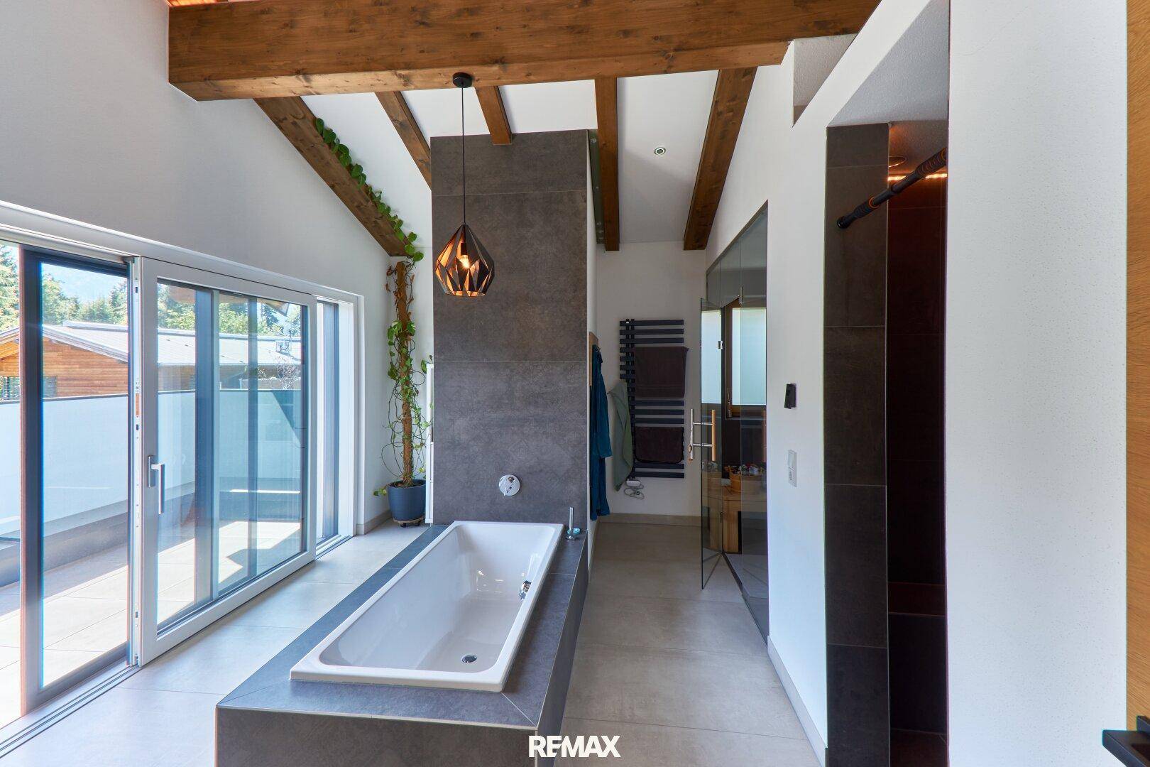 Modernes Badezimmer mit Badewanne, Holzbalken und Zugang zu einer Außenterrasse.