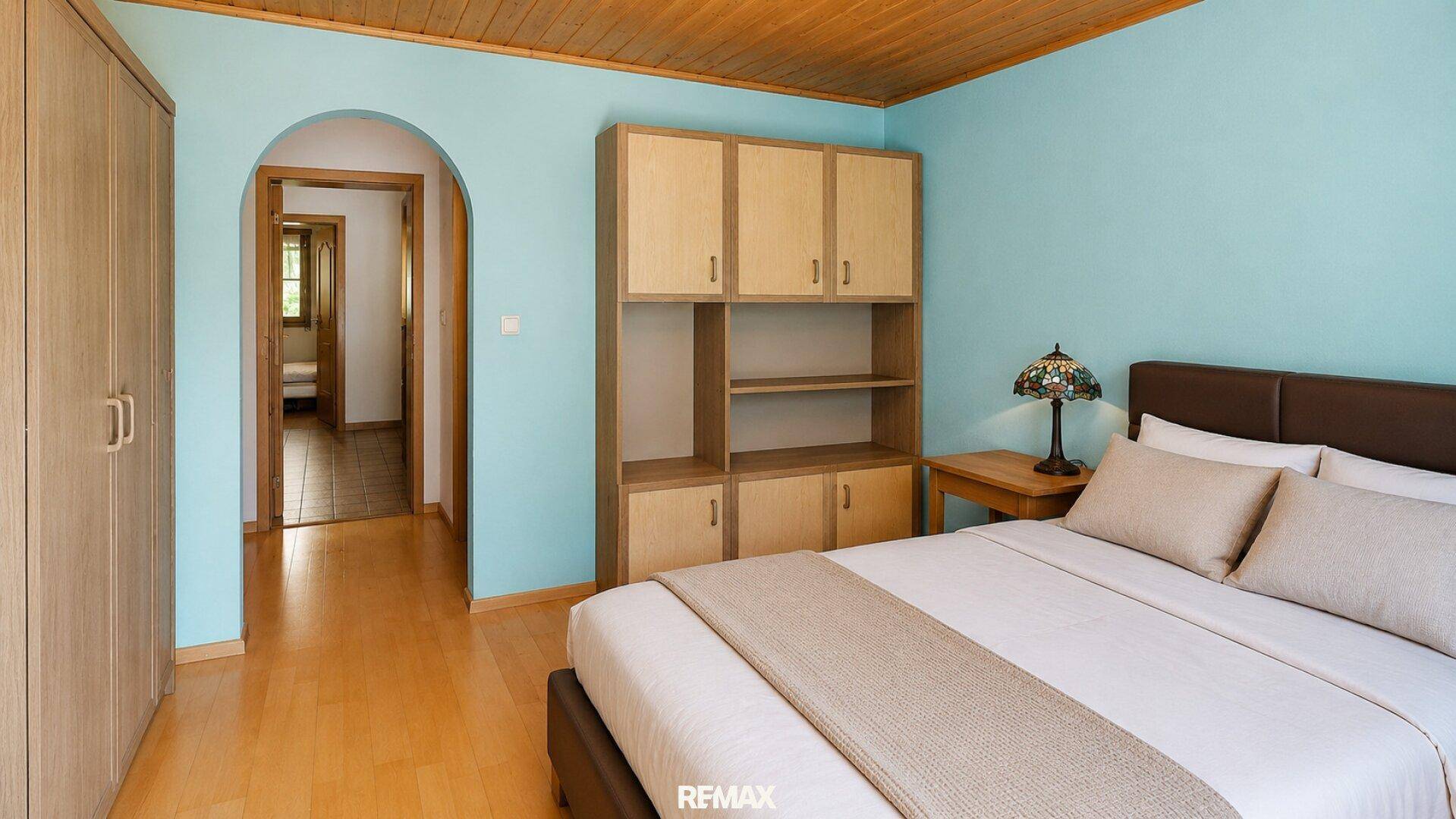 Schlafzimmer mit Doppelbett, hellblauen Wänden, Holzdecke und praktischen Einbauschränken.
