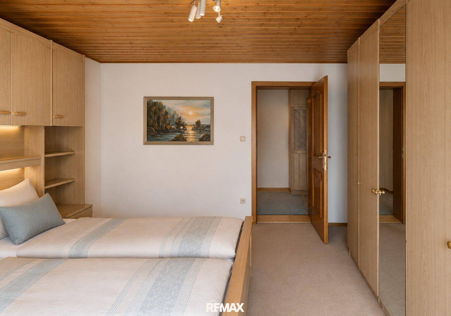 Schlafzimmer mit zwei Einzelbetten, Holzschränken und Zugang zu einem weiteren Raum.