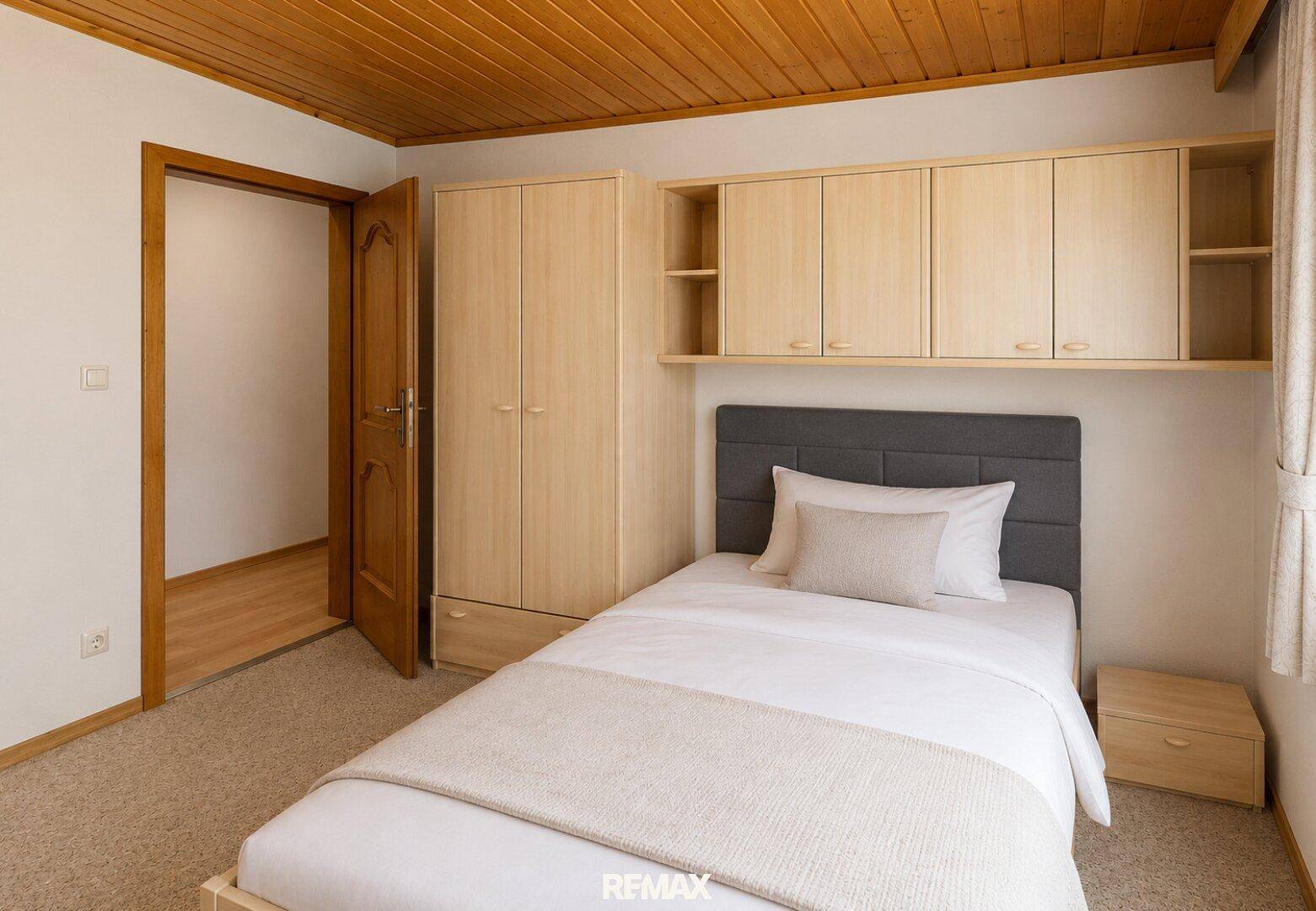 Schlafzimmer mit Einzelbett, Kleiderschrank, Hängeschränken und traditioneller Holzdecke.