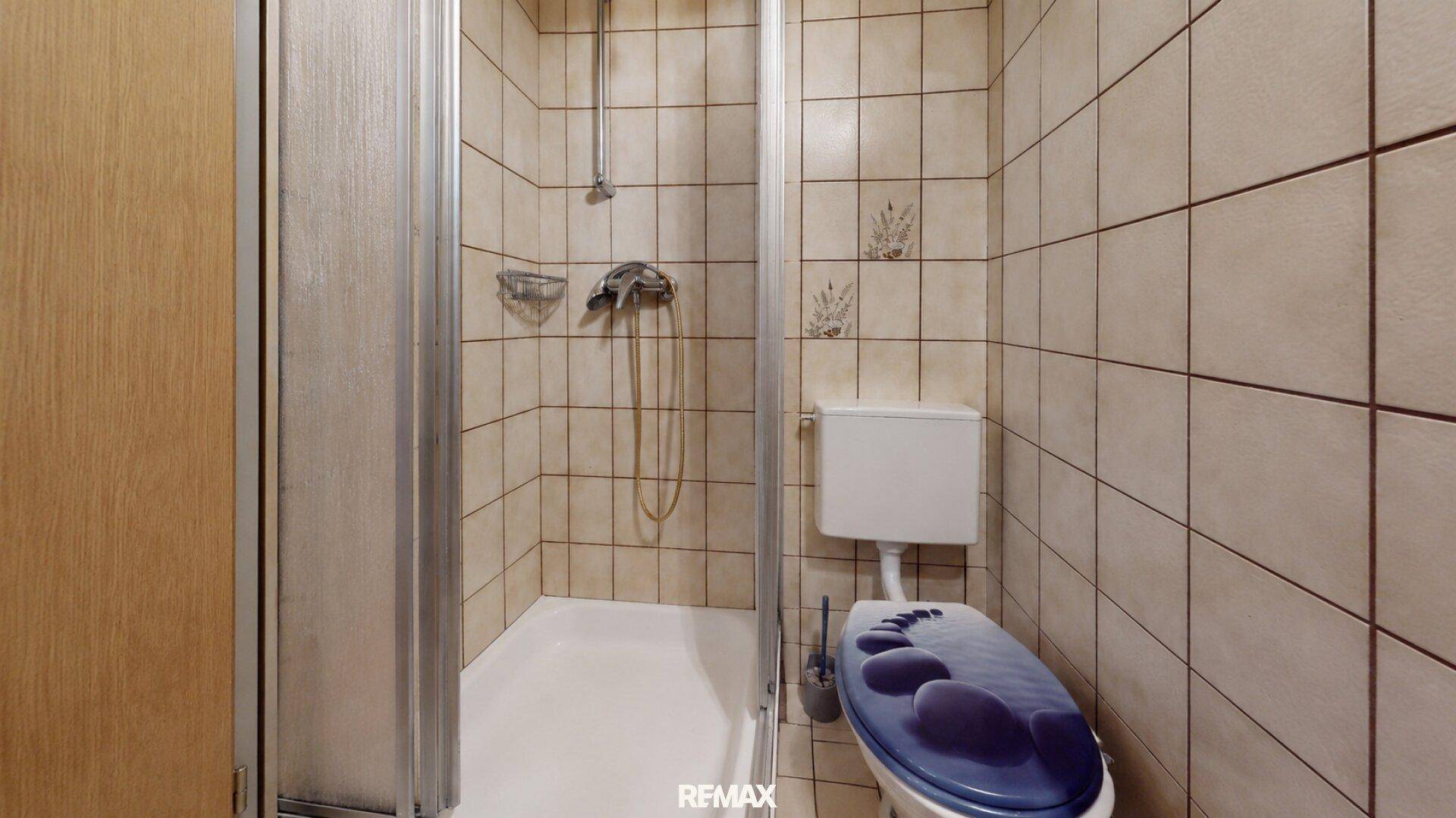 Kleines Badezimmer mit Duschkabine und Toilette, komplett gefliest in beigen Tönen.