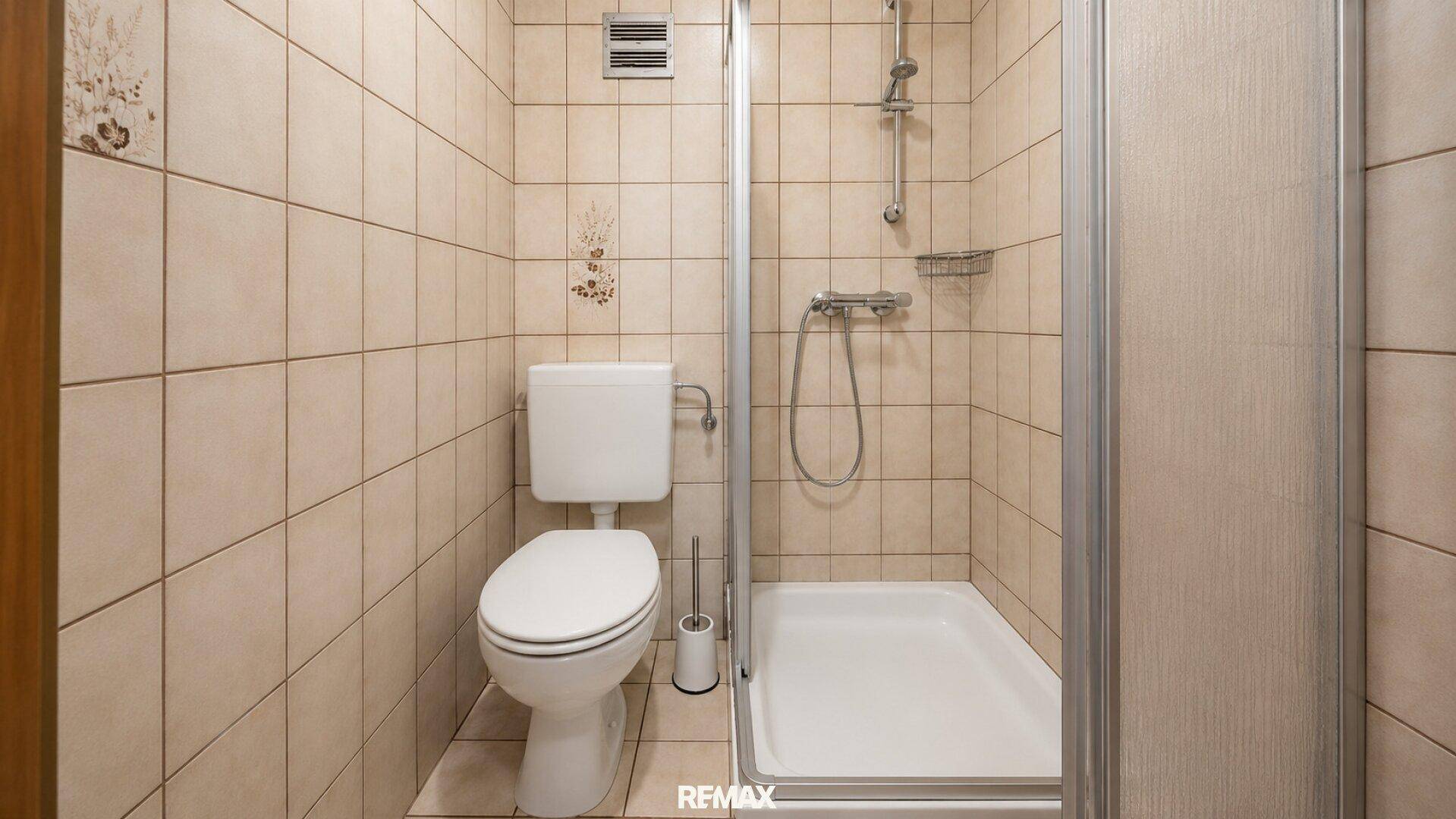Funktionales Badezimmer mit Duschkabine und WC, vollständig mit hellen Fliesen ausgestattet.