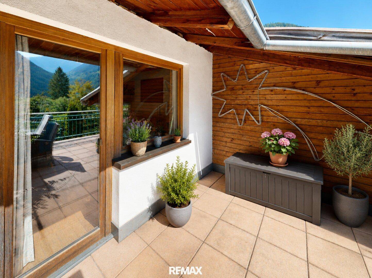 Kleiner Balkon mit Fliesenboden, Holzwand und Blick auf die umliegende Berglandschaft.