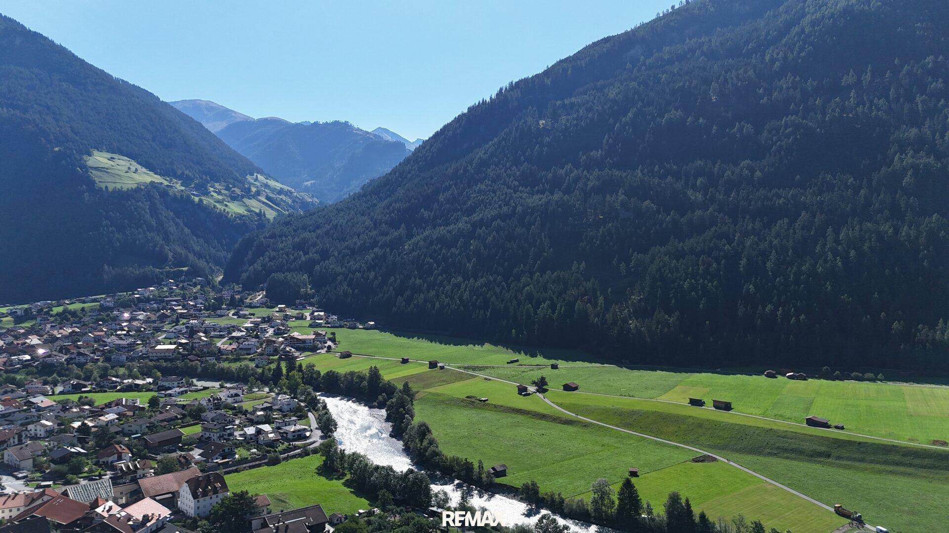 Weitläufige Luftaufnahme eines Flusstals mit grünen Feldern und einem Dorf am Ufer.