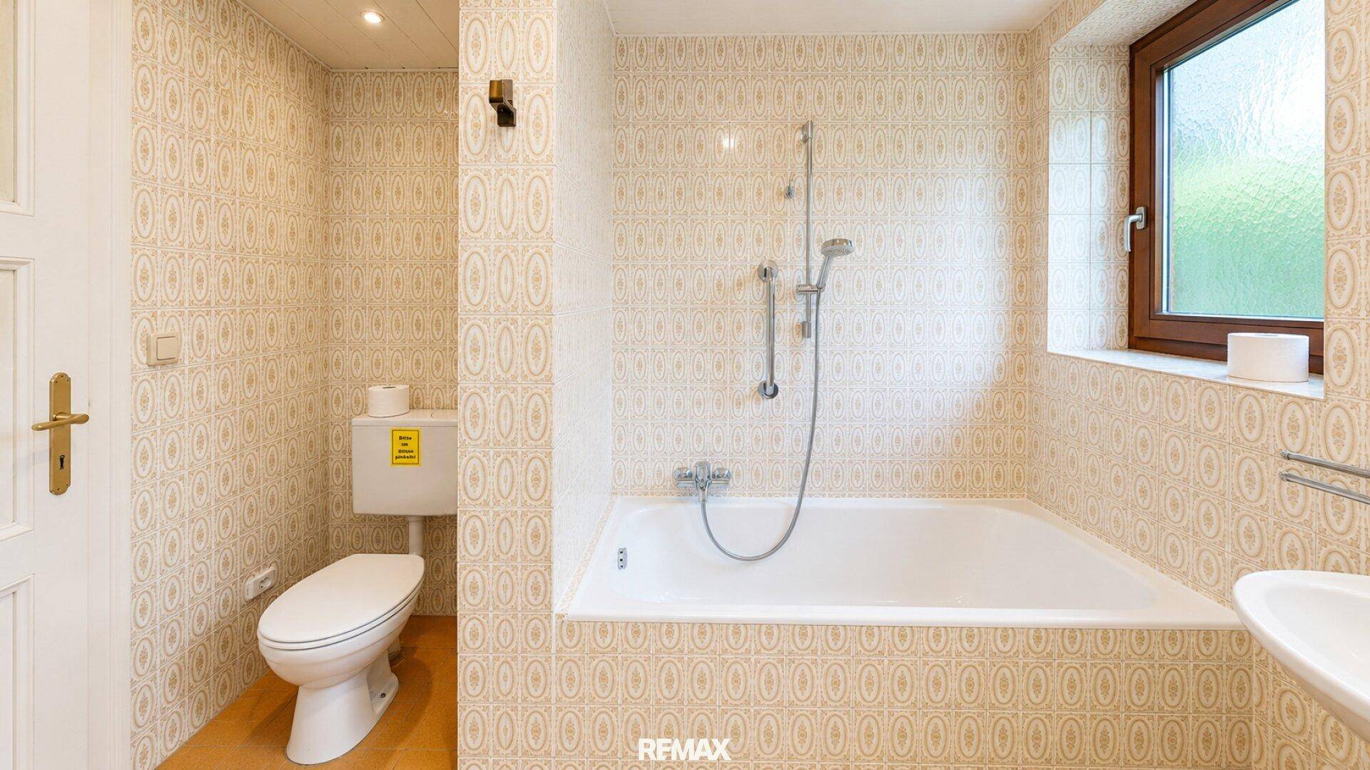 Badezimmer im Retro-Stil mit Badewanne, WC und Fenster, komplett gefliest.