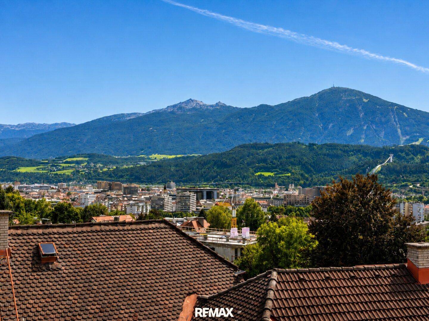 Weitläufiger Blick über die Stadt und die umliegende Berglandschaft unter blauem Himmel.