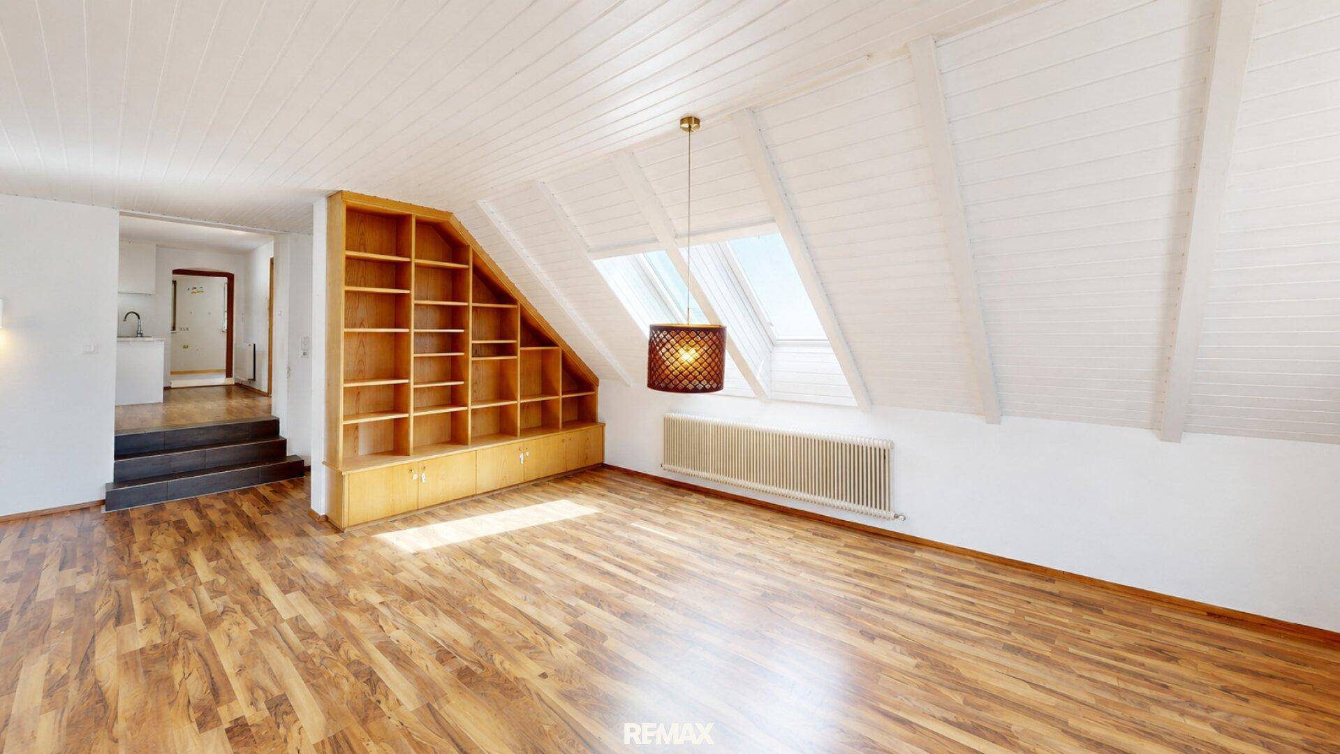 Großzügiger Wohnbereich im Dachgeschoss mit Holzboden, Einbauregal und Dachfenstern.