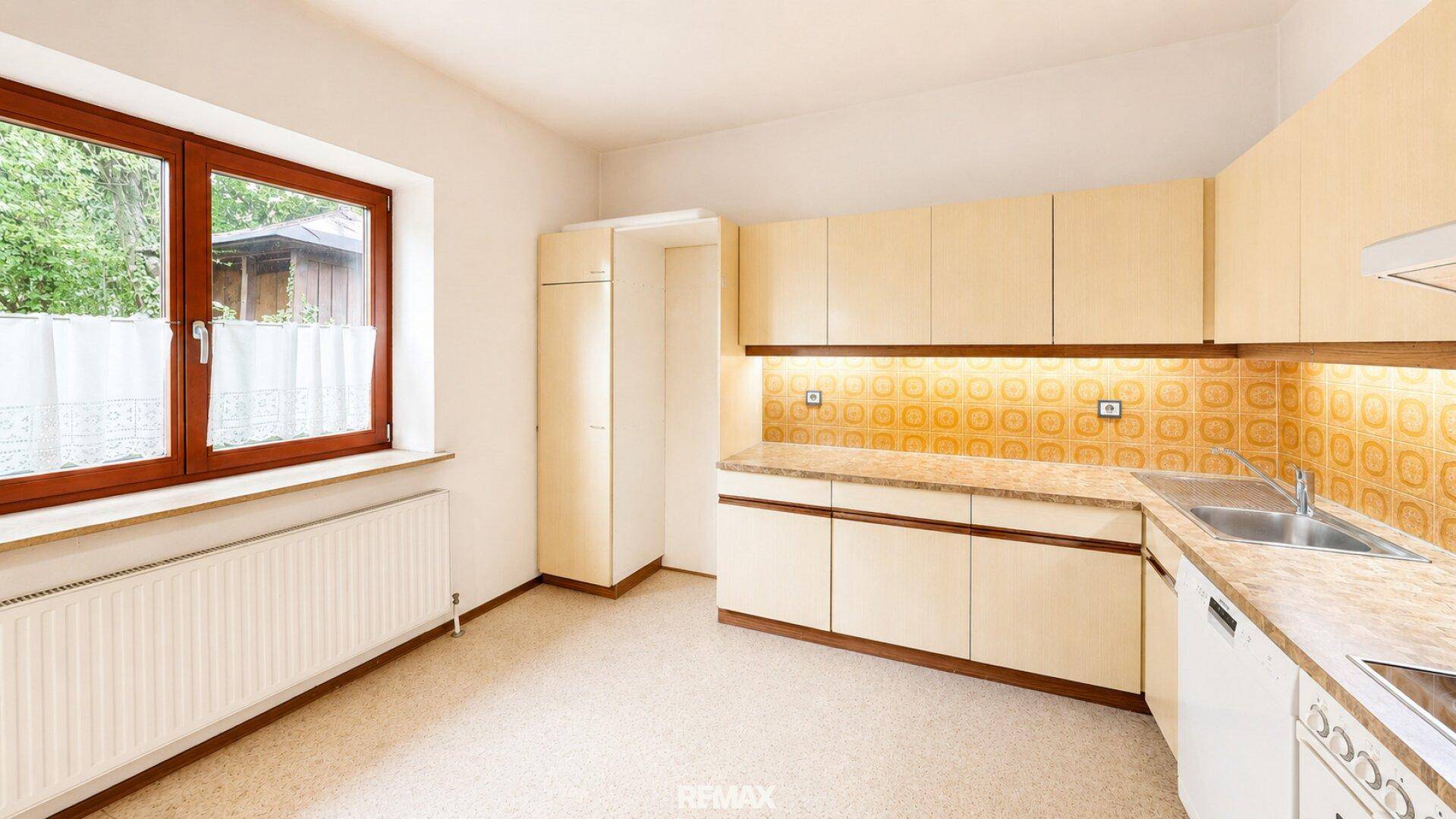 Helle Küche mit Einbauschränken, Fenster und Platz für einen Essbereich.