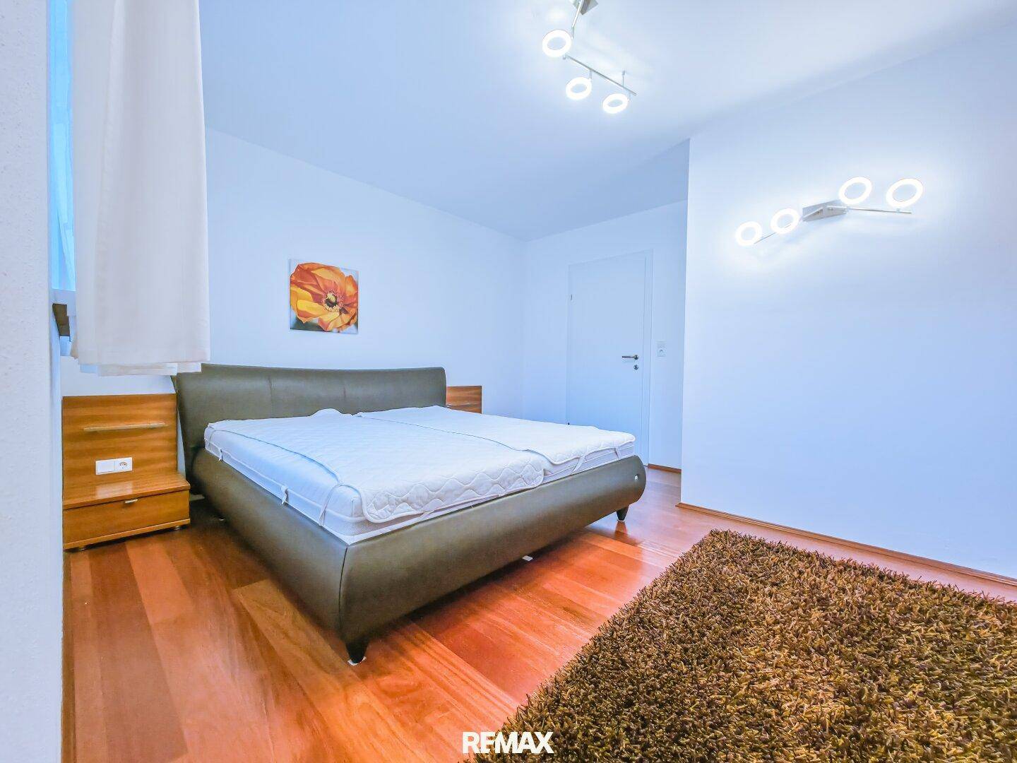 Schlafzimmer mit Doppelbett, Holzboden und moderner Beleuchtung.