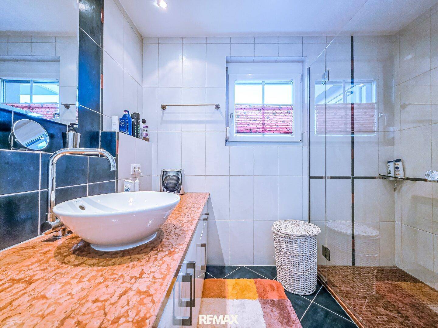 Modernes Badezimmer mit Waschtisch, Dusche und Fenster, gefliest.