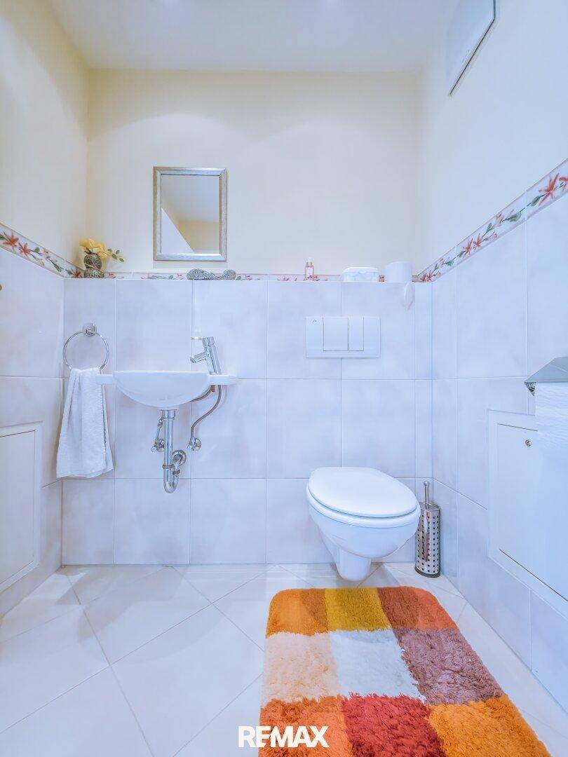 Separates Gäste-WC mit Wand-WC, Waschbecken und Fliesenboden.