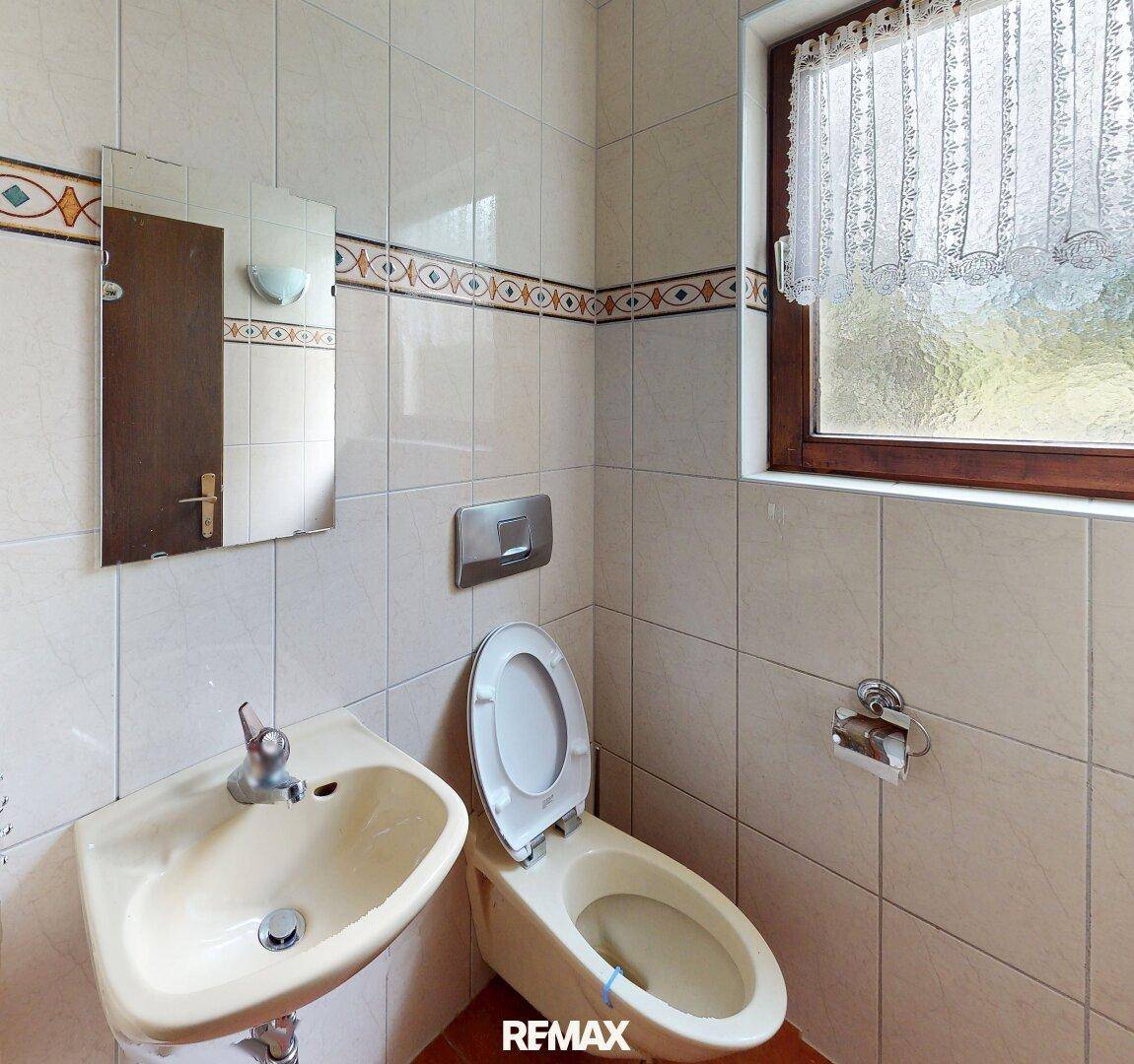 Kleines Gäste-WC mit Fenster, Waschbecken und Wand-WC in hellem Design.