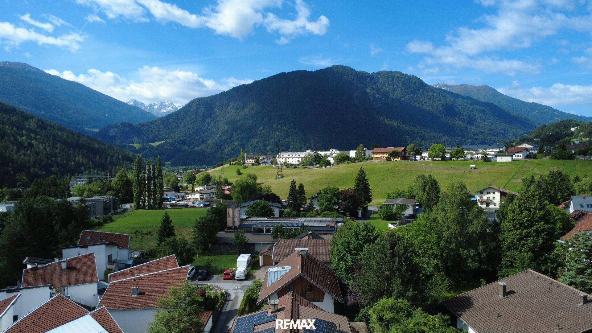 Weitläufige Ansicht eines Dorfes mit Häusern und grünen Feldern, eingebettet in eine Berglandschaft.