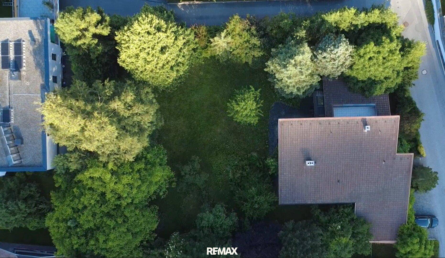 Luftaufnahme eines Grundstücks mit einem Haus, umgeben von einer großen Rasenfläche und vielen Bäumen.