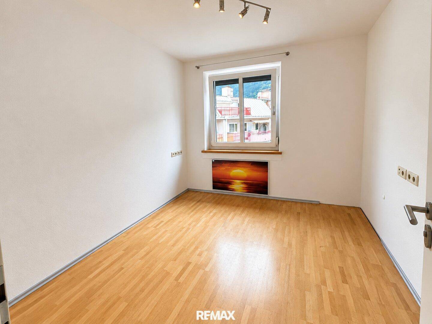 Helles, leeres Zimmer mit Parkettboden und Fenster, ideal für Schlaf- oder Arbeitsbereich.