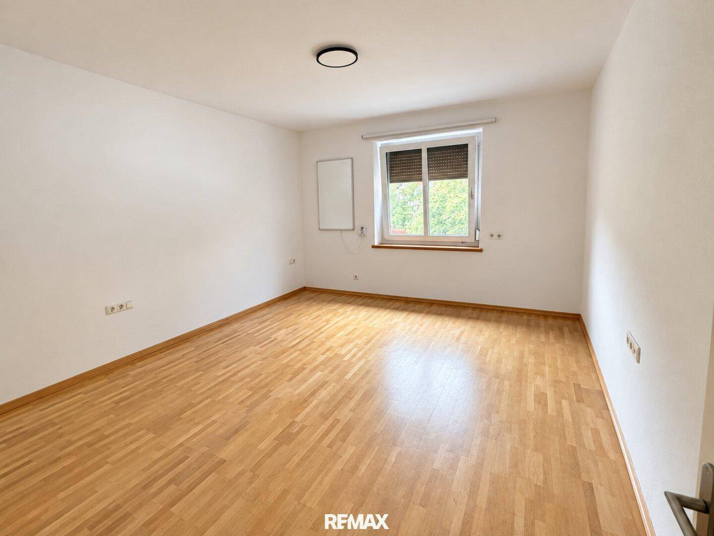 Leeres Zimmer mit hellem Parkettboden und einem Fenster, bereit zur individuellen Gestaltung.