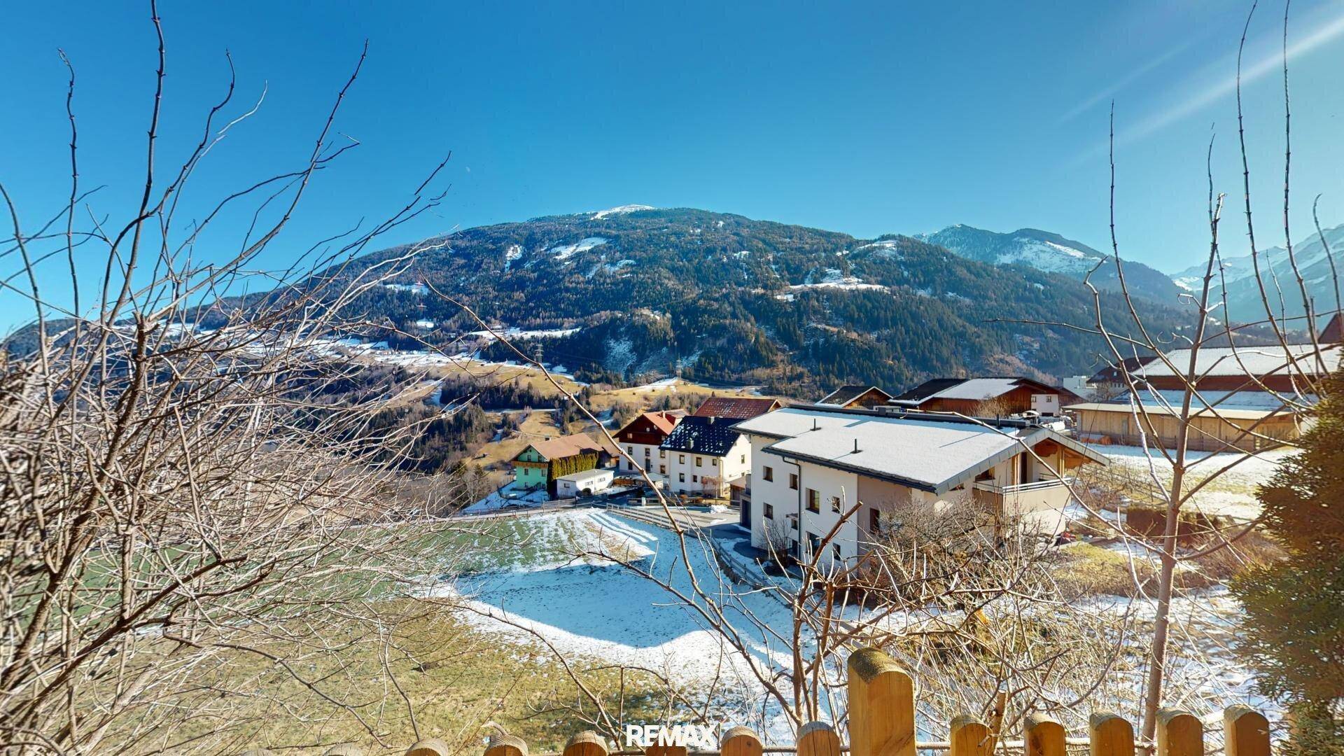 Panoramablick auf die verschneite Berglandschaft und umliegende Häuser in der Ferne.