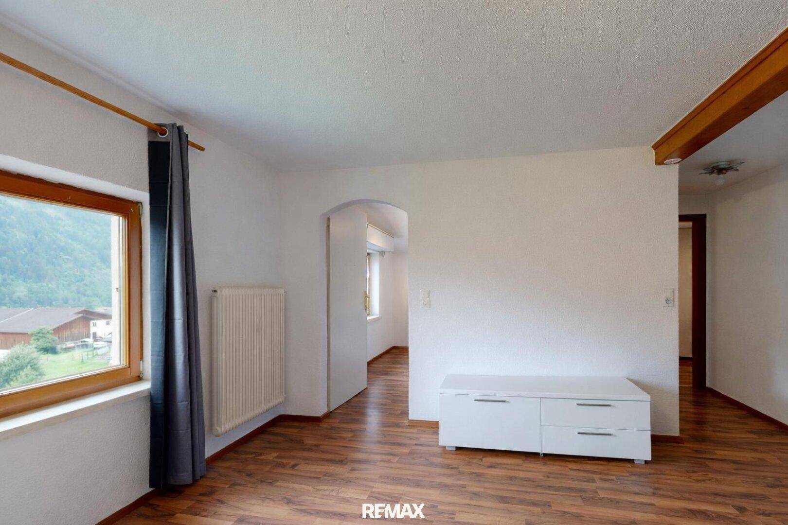 Helles Wohnzimmer mit Laminatboden, Heizkörper und Fenster mit Blick ins Grüne.