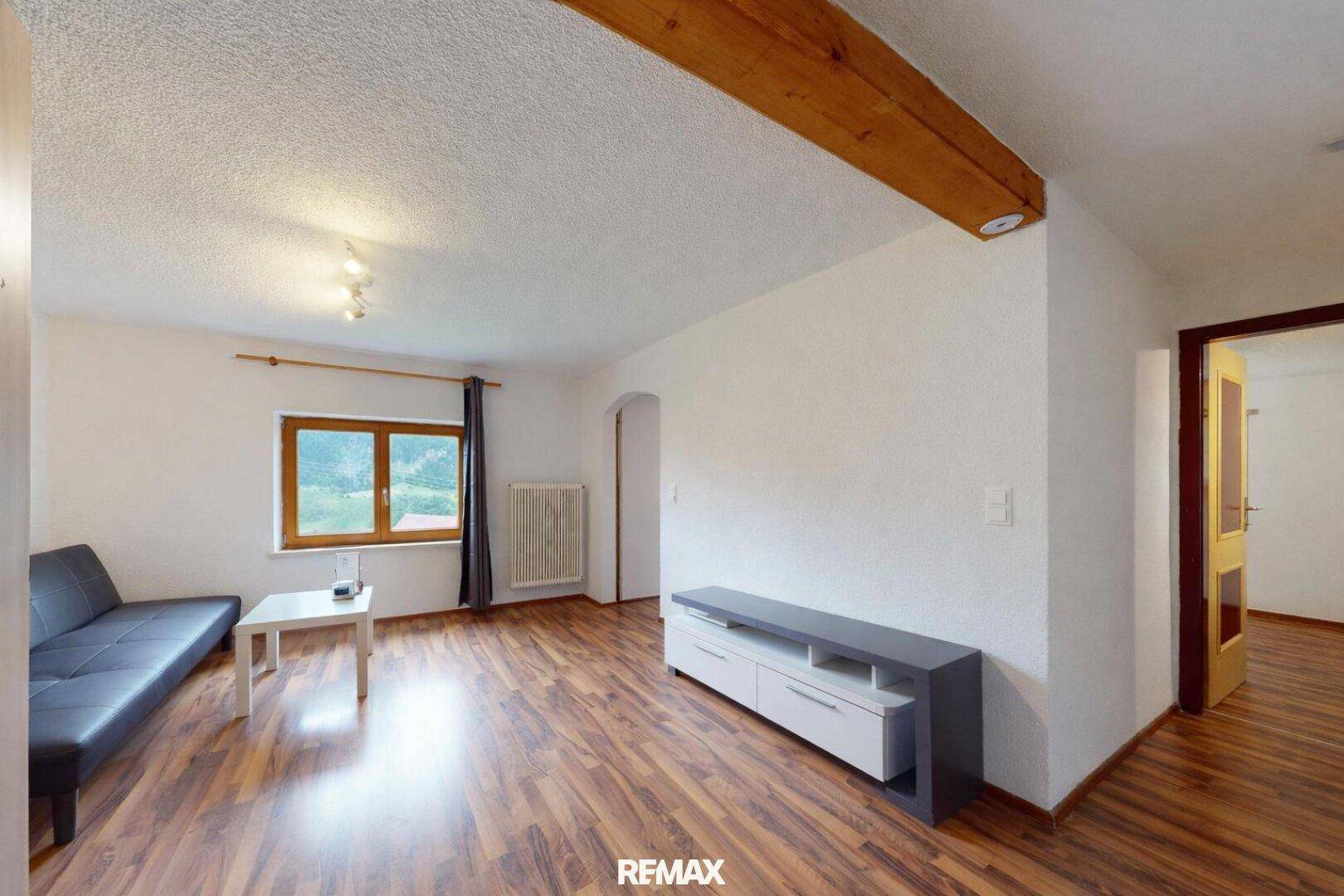 Geräumiges Wohnzimmer mit Laminatboden, Sofa und sichtbaren Holzbalken an der Decke.