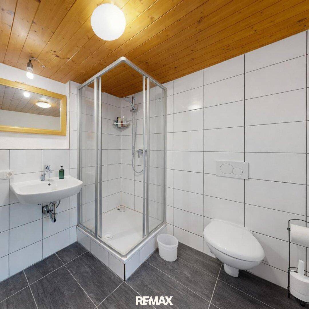 Helles Badezimmer mit Duschkabine, WC und einer rustikalen Holzdecke.