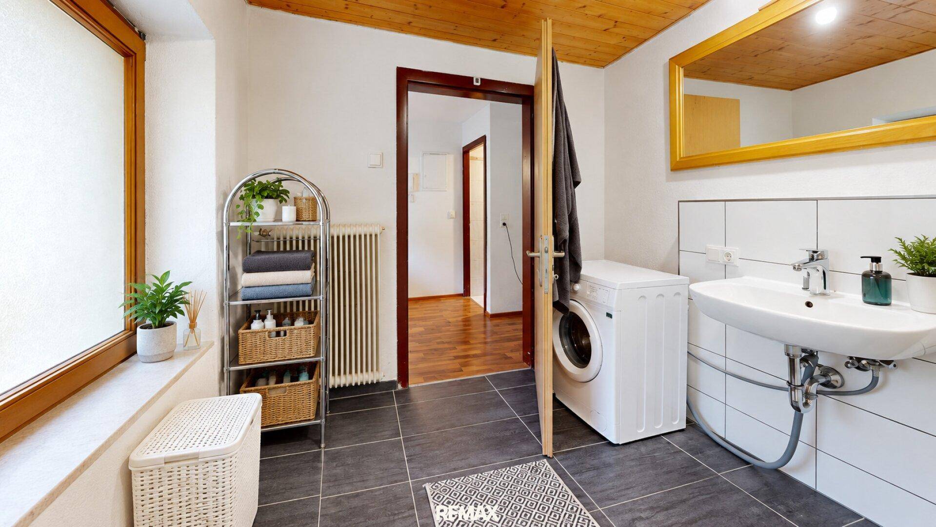 Badezimmer mit Waschmaschine, Waschbecken und Fenster für ausreichend Tageslicht.