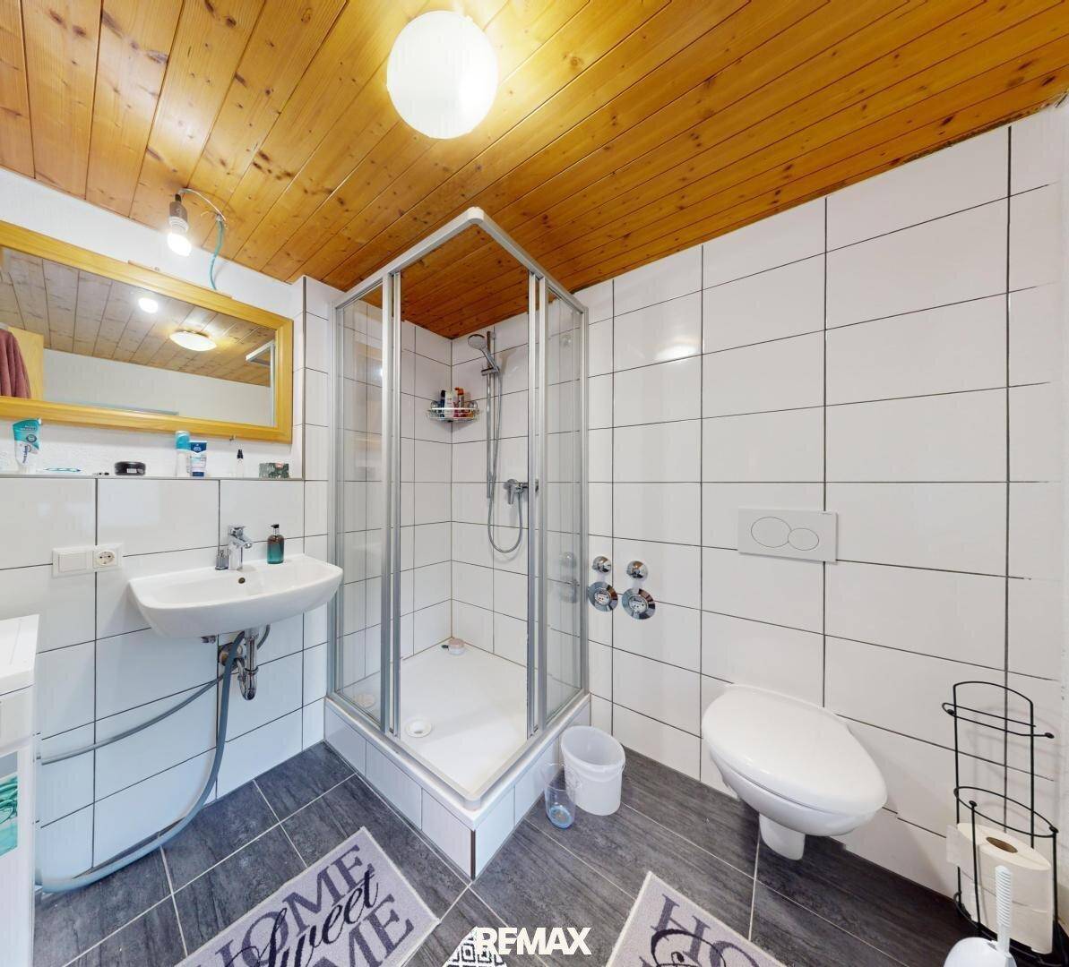 Badezimmer mit Duschkabine, Waschbecken und einer warmen Holzdecke.
