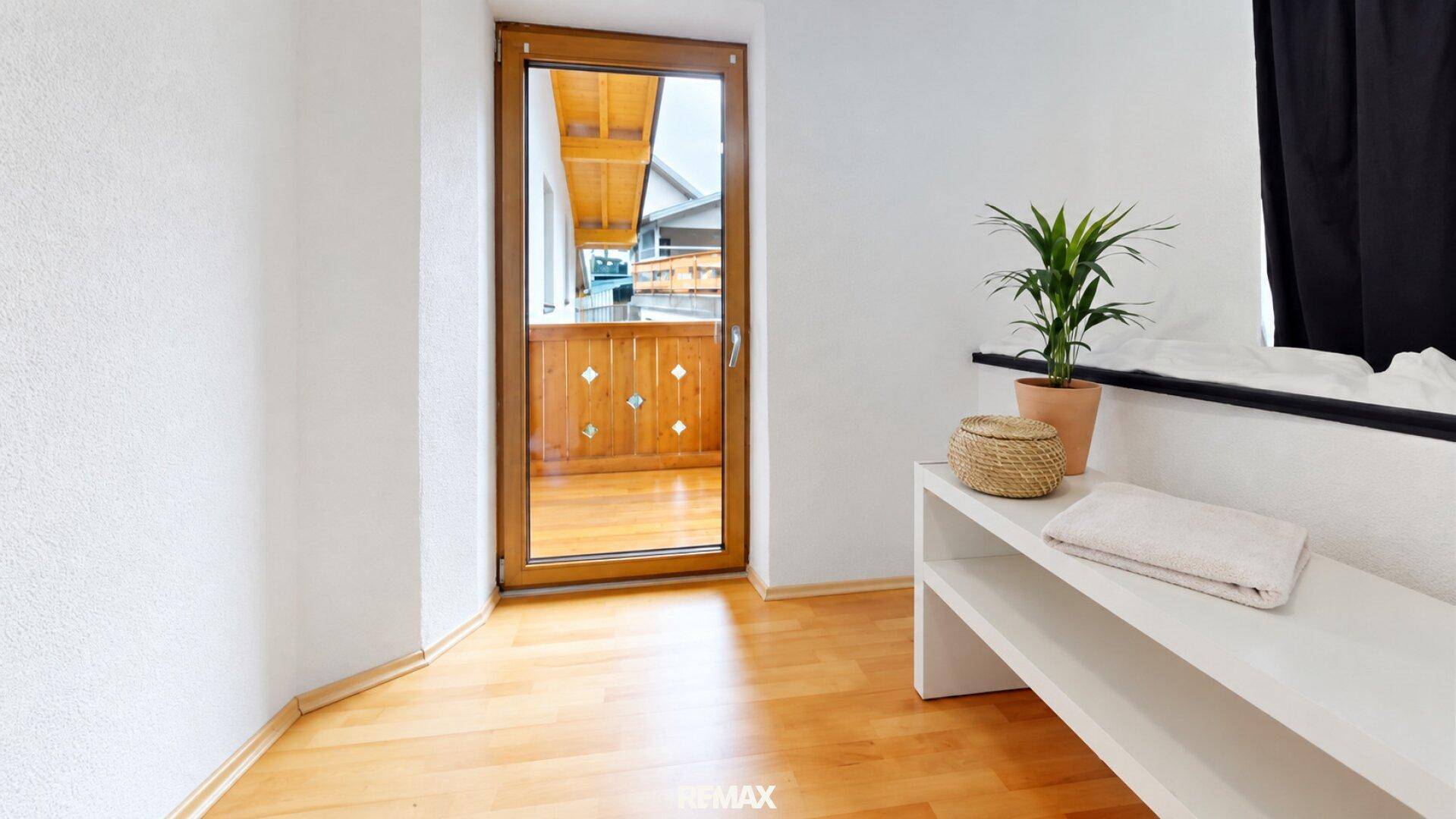 Schlafzimmer mit Holzbalkon-Zugang und hellem Laminatboden, gut beleuchtet.