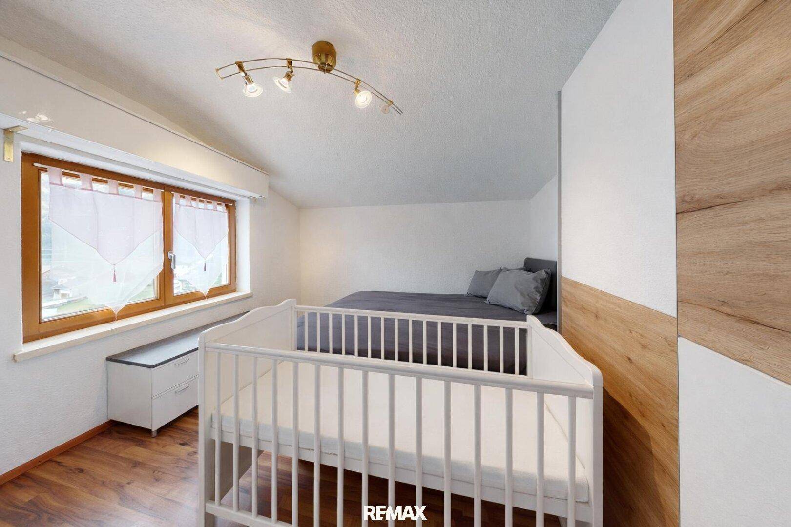 Schlafzimmer mit Babybett, Doppelbett und einer gemütlichen Dachschräge.