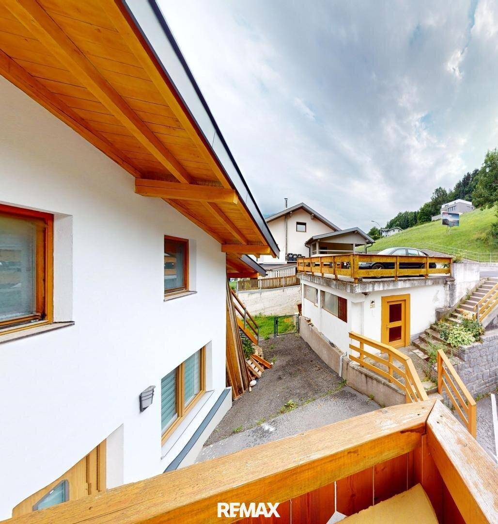 Balkon mit Holzgeländer und Blick auf die umliegende Bebauung und grüne Hügel.