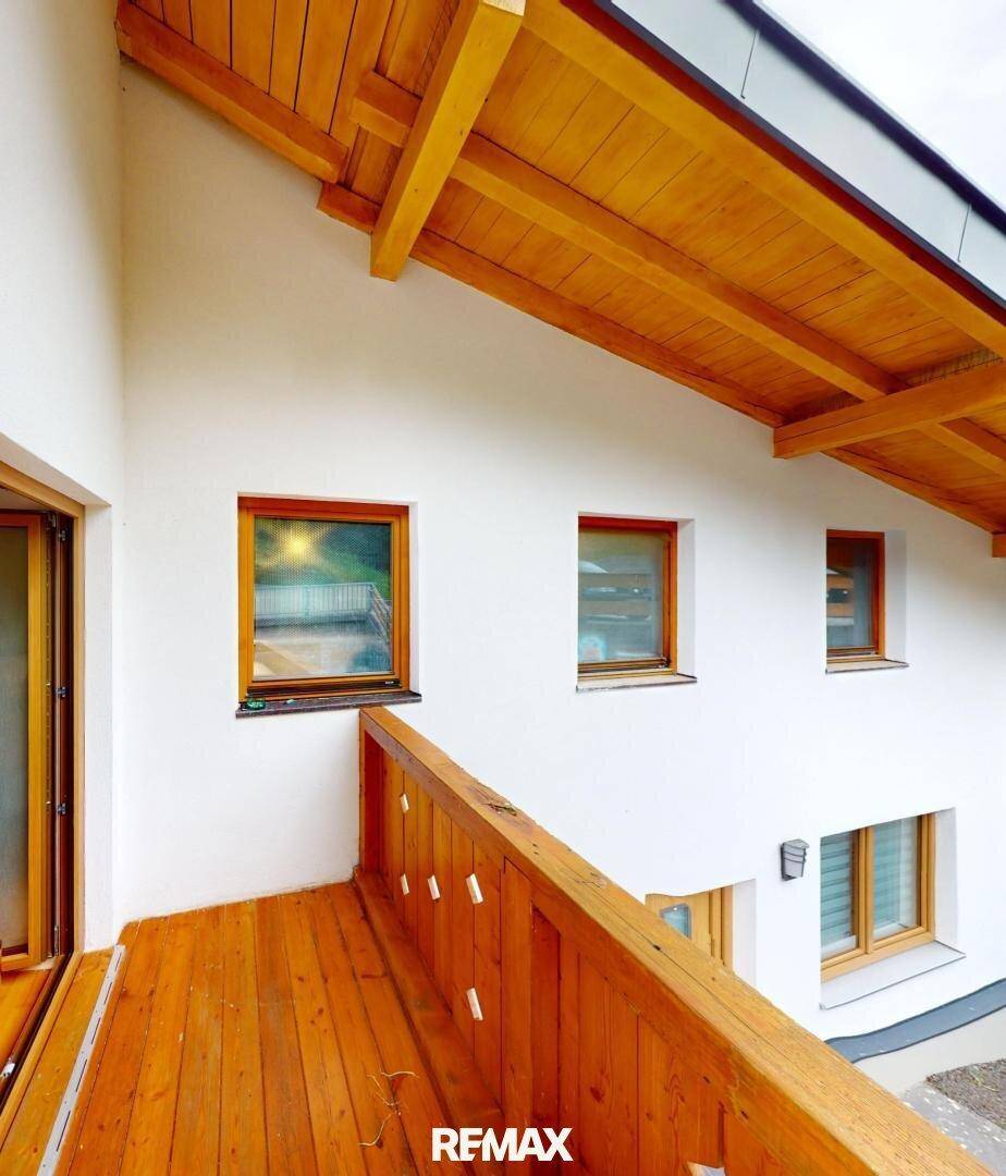 Holzverkleideter Balkon mit Blick auf die weiße Fassade des Hauses und die Umgebung.